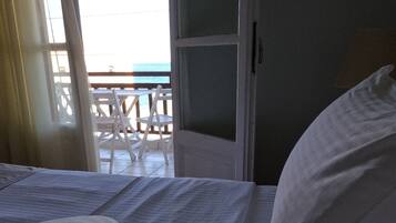 A bed with white linens and striped pillows, a wooden headboard, and a view of an outdoor deck with white chairs.