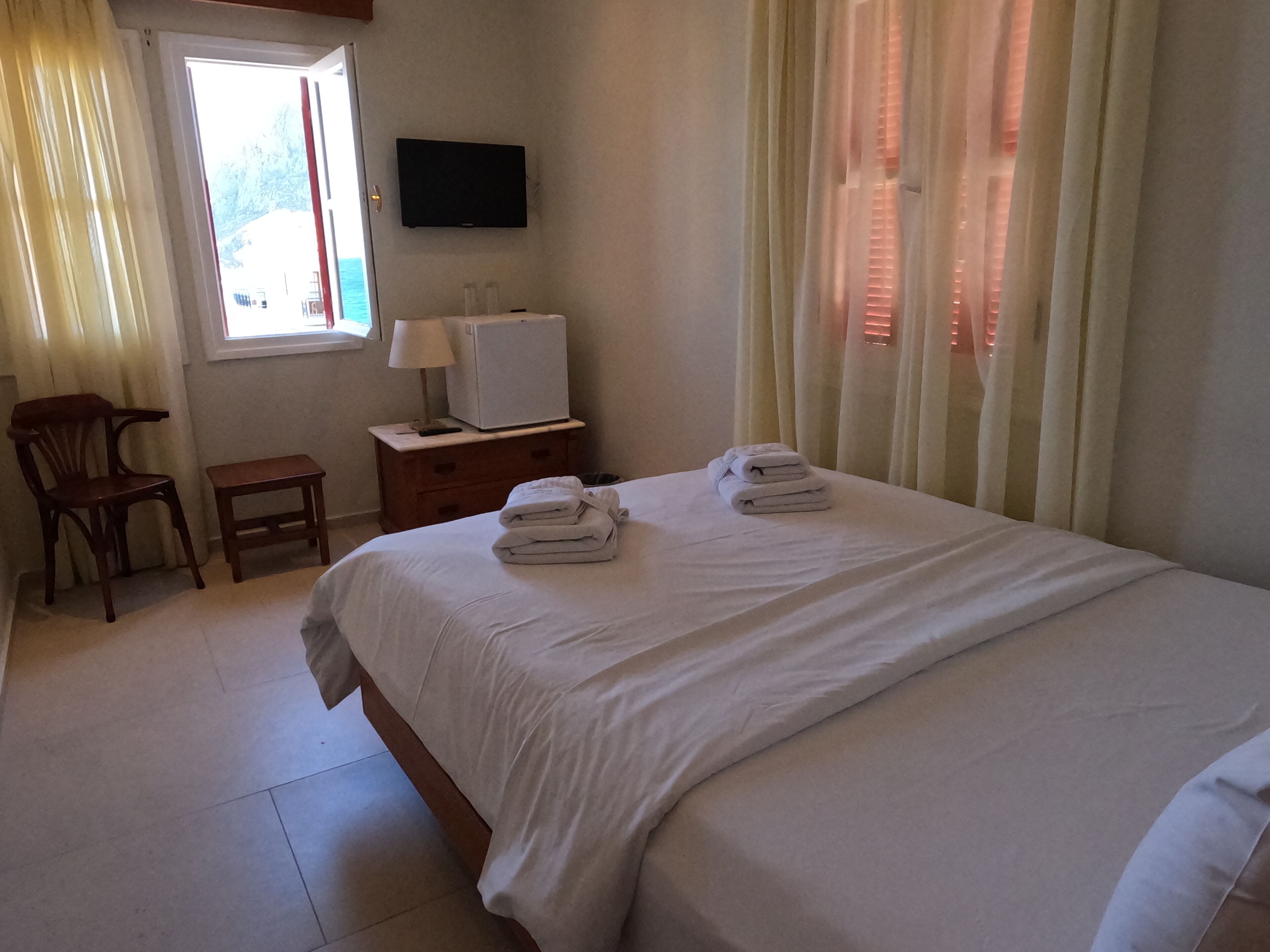 Une chambre d’hôtel avec un lit, une télévision, un bureau avec une lampe, une chaise et une fenêtre avec des rideaux.