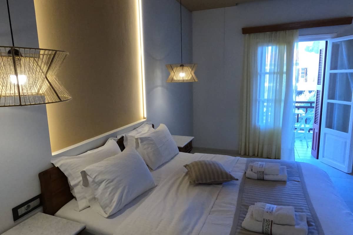 A hotel room with a neatly made bed, two bedside tables, a hanging lamp, and a view of the outside.