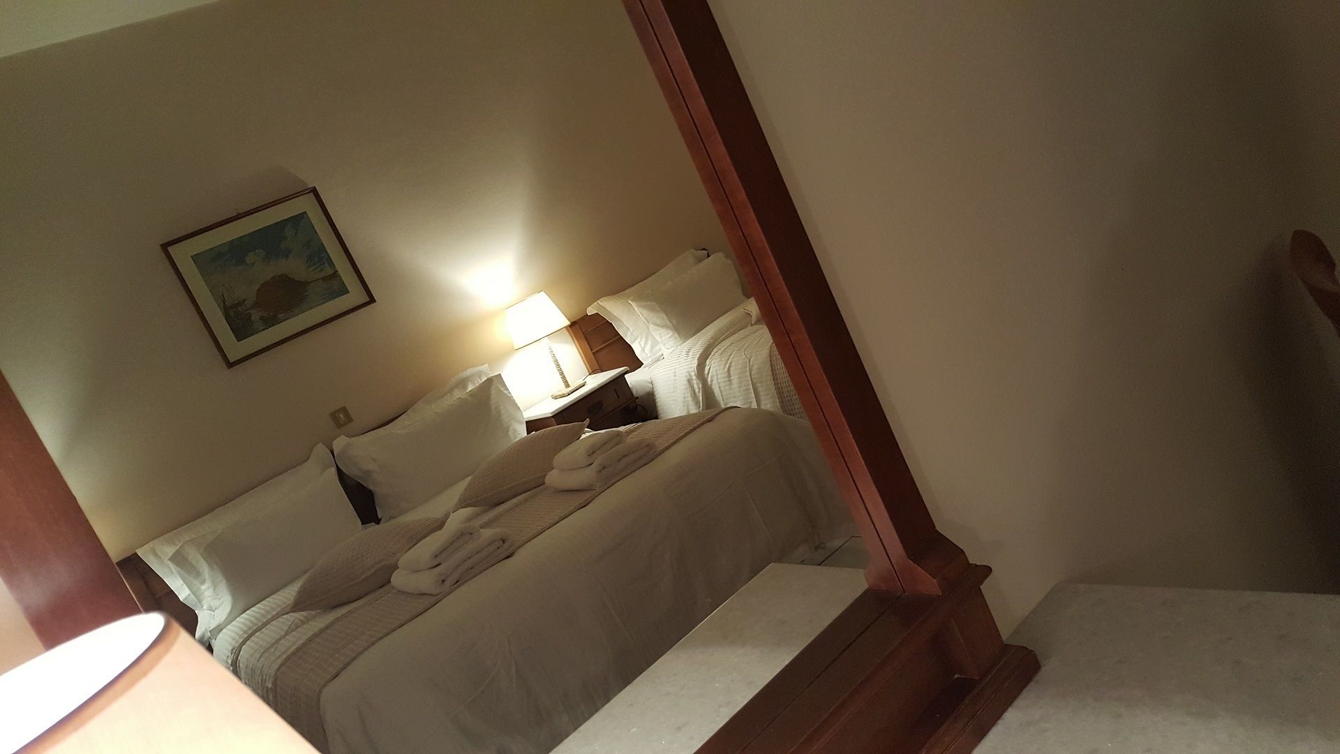 A bedroom with a four-poster bed, a bedside table with a lamp, and a painting on the wall.