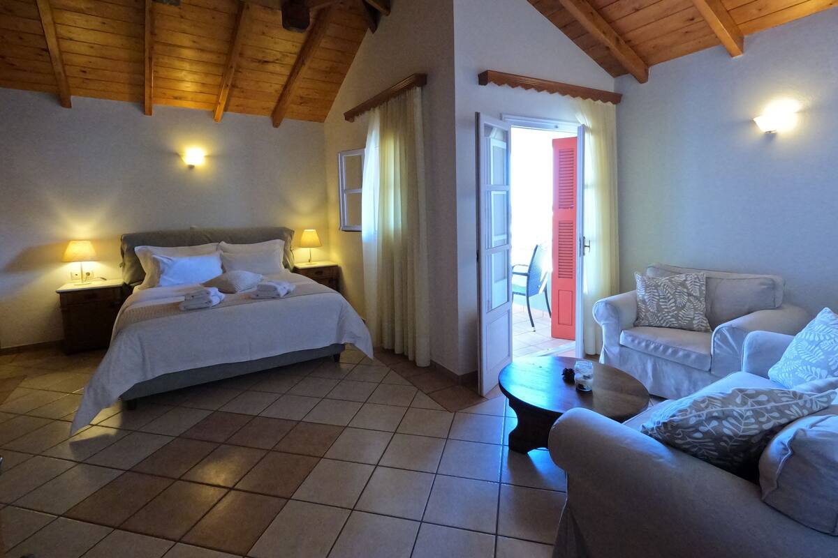 A hotel room with a bed, a sofa, a small table, and a door leading to an outdoor area.