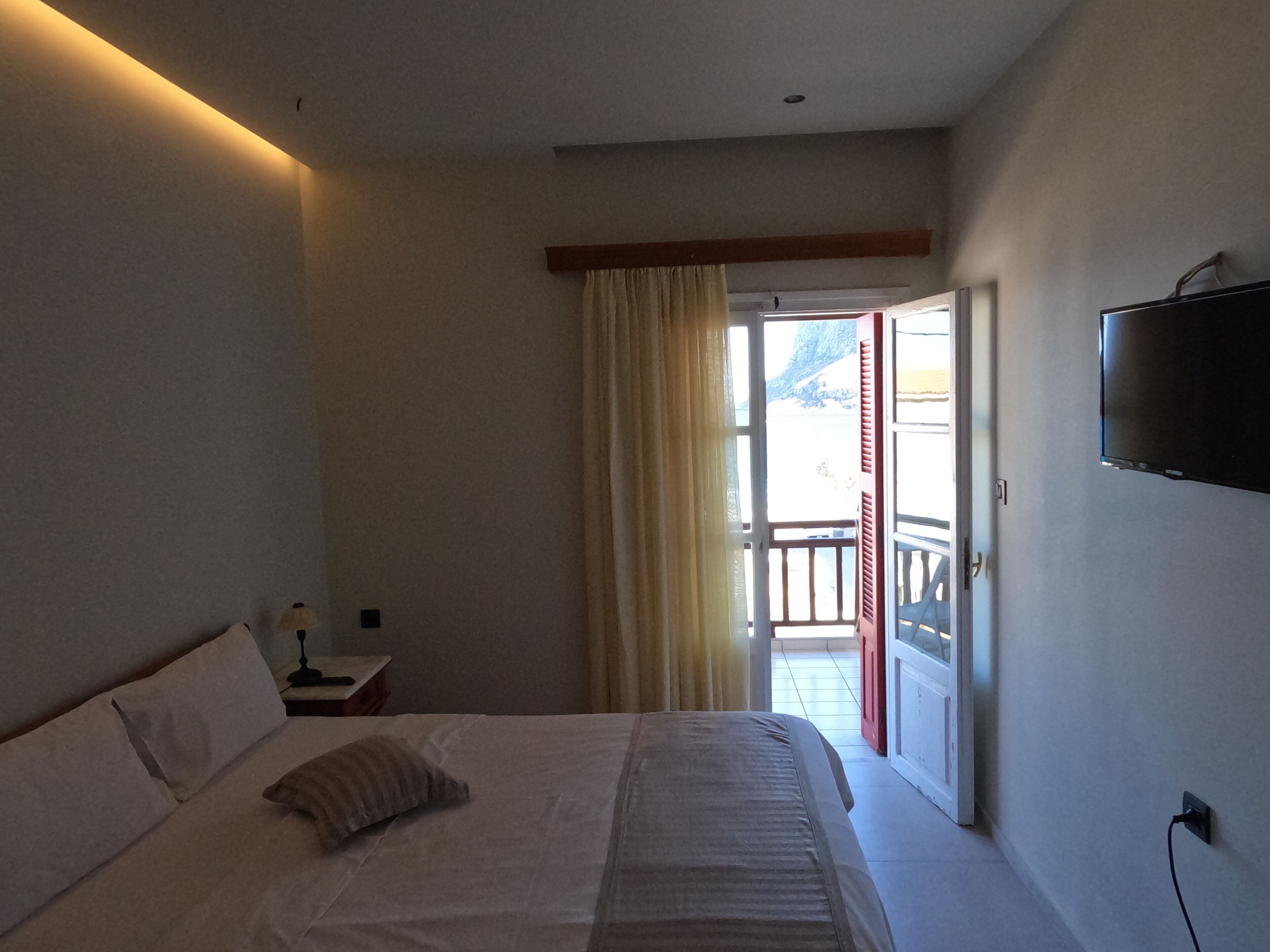 Un dormitorio con cama, mesita de noche, televisor montado en la pared y puerta corrediza de vidrio que da a un espacio exterior.
