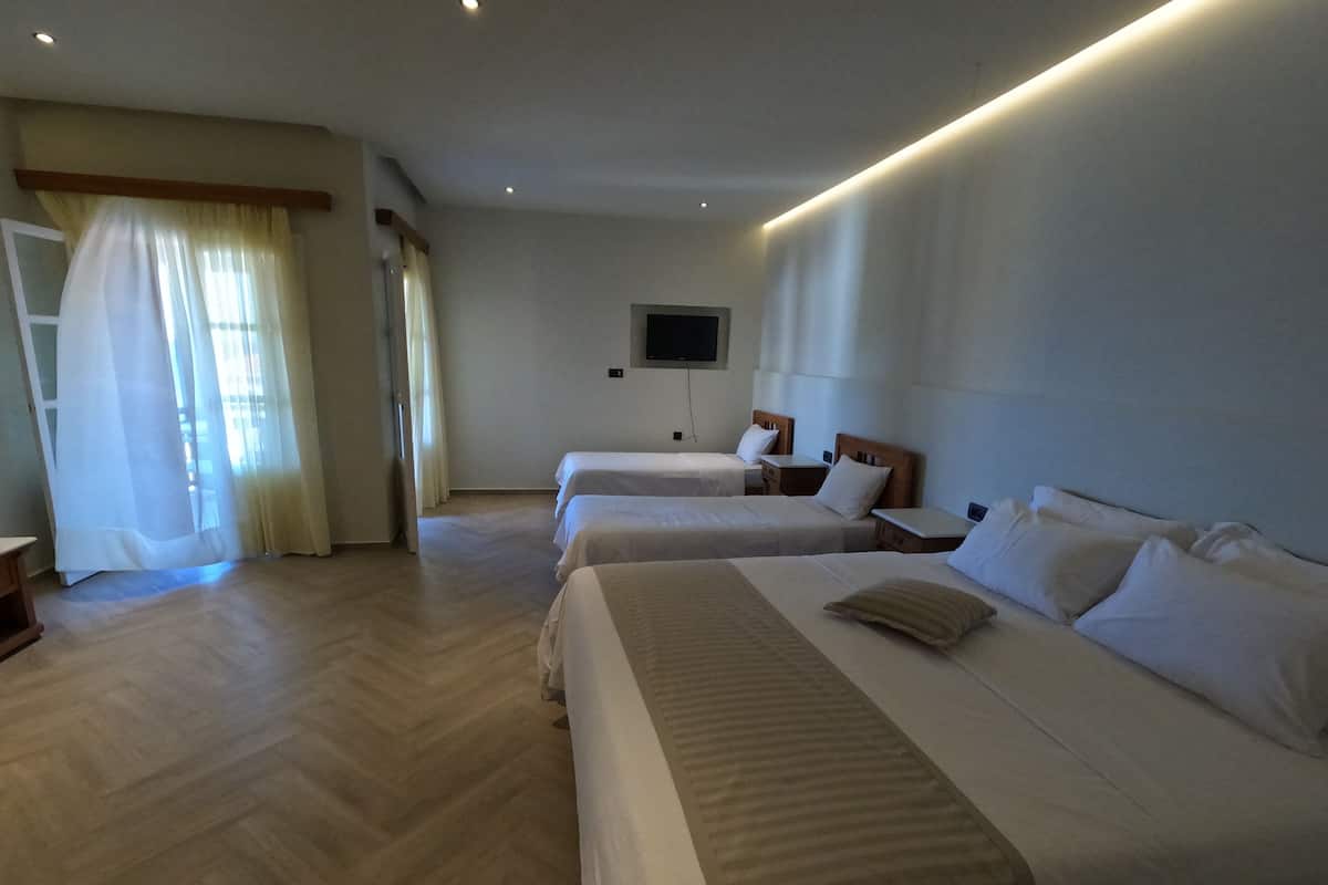A hotel room with two beds, a flat-screen TV mounted on the wall, and a wooden floor.