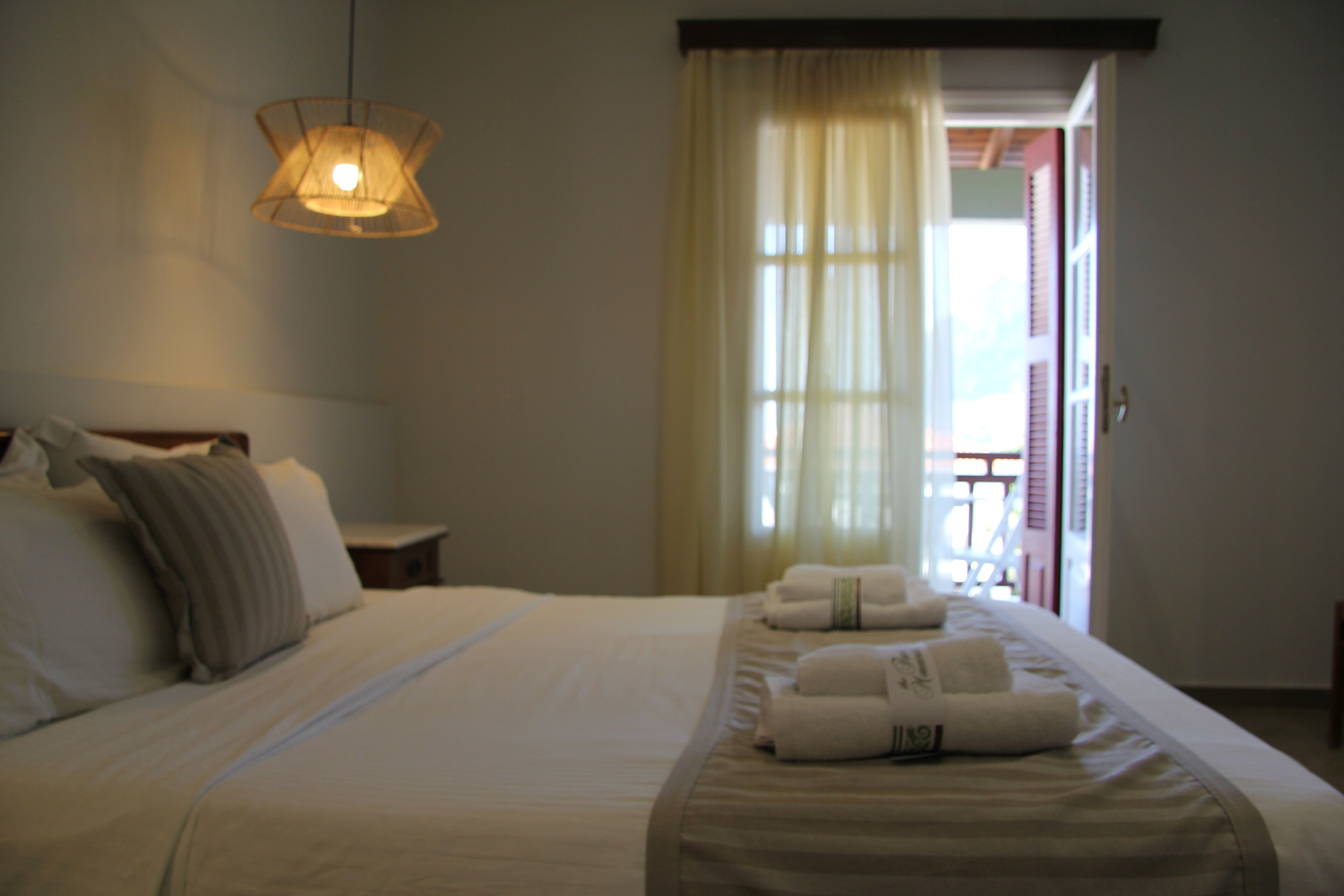 Una camera d'albergo con un letto, cuscini, un comodino, una lampada e una finestra con tende.