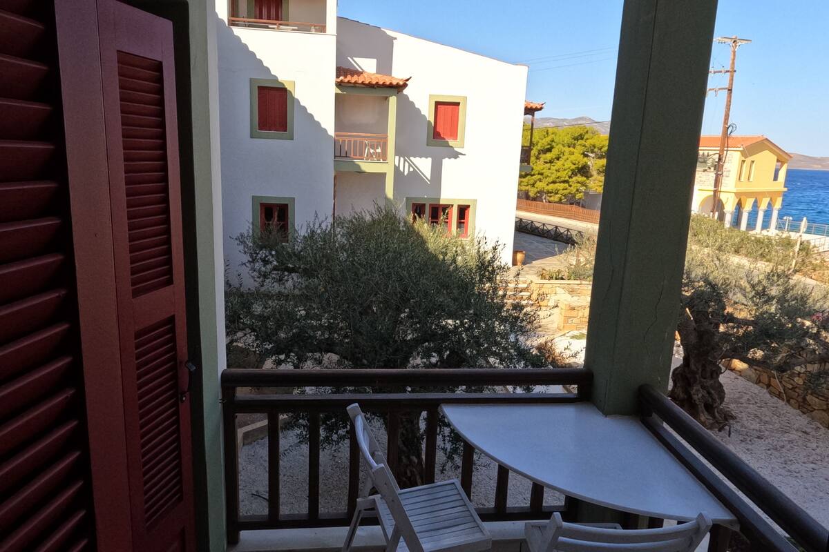 A balcony with a table and two chairs, overlooking a beach and buildings.