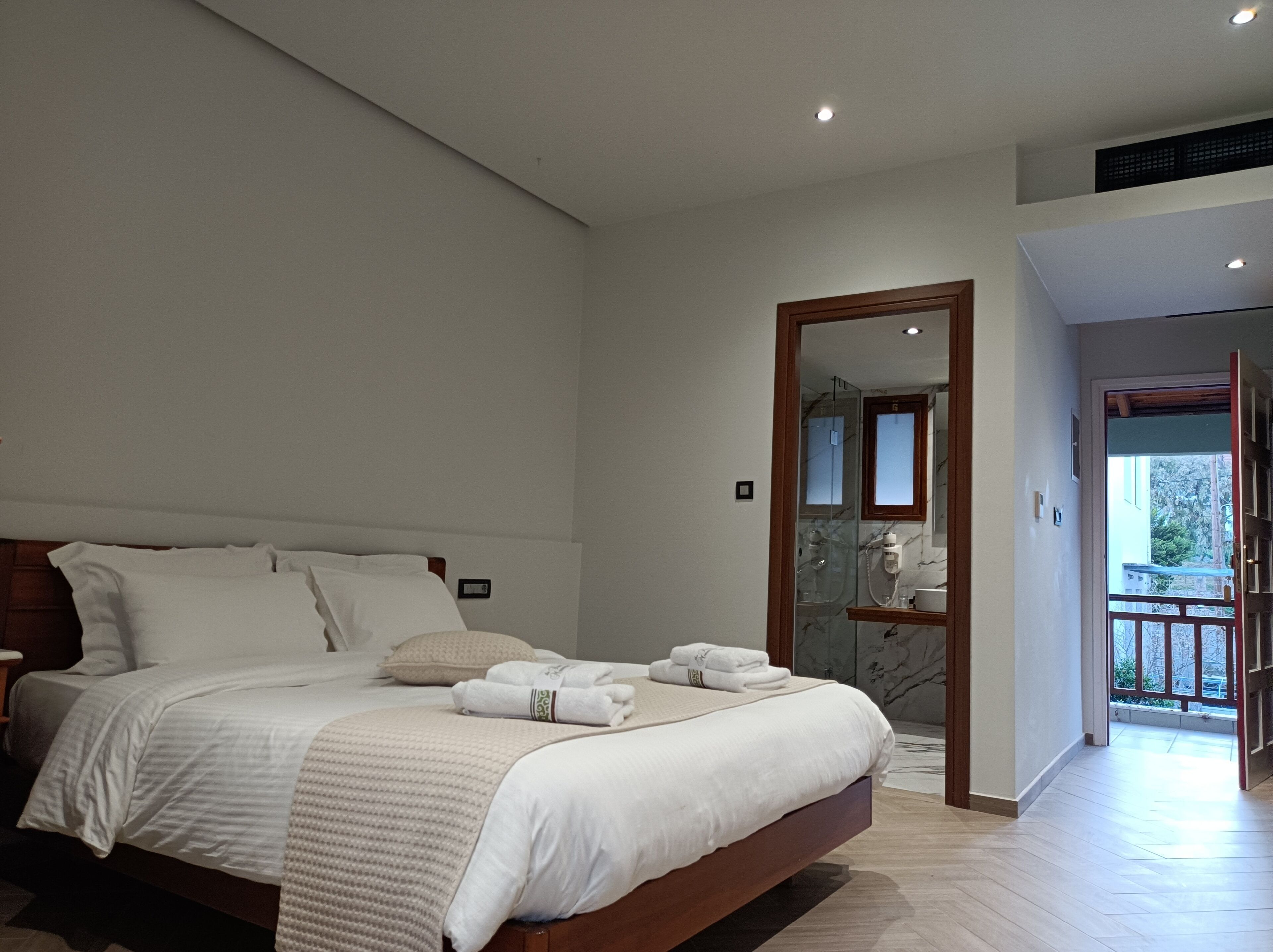 A modern bedroom with a large bed, a wooden headboard, and a glass shower area visible through an open door.