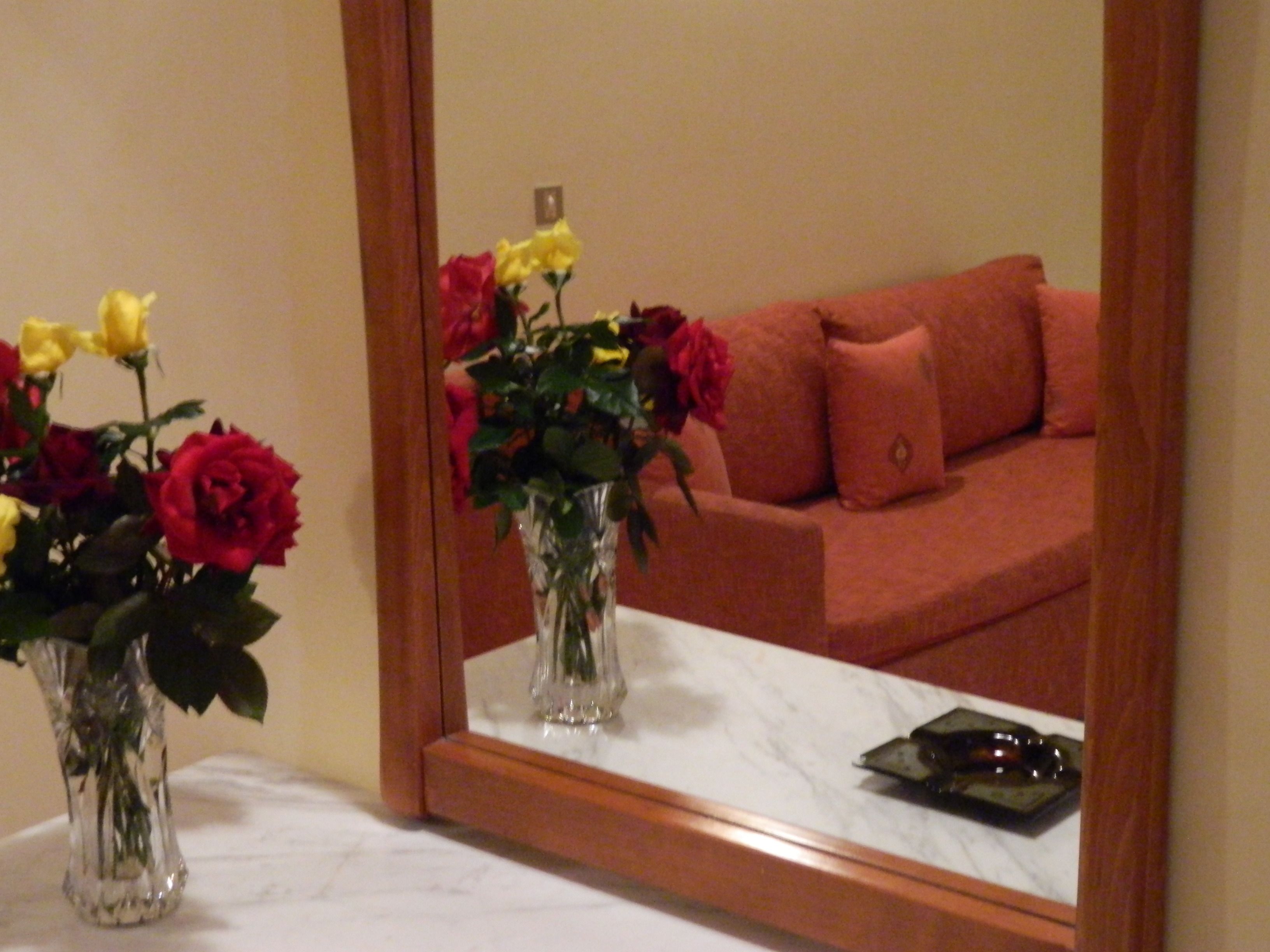 A mirror reflecting a room with a sofa and a vase of flowers on a table.