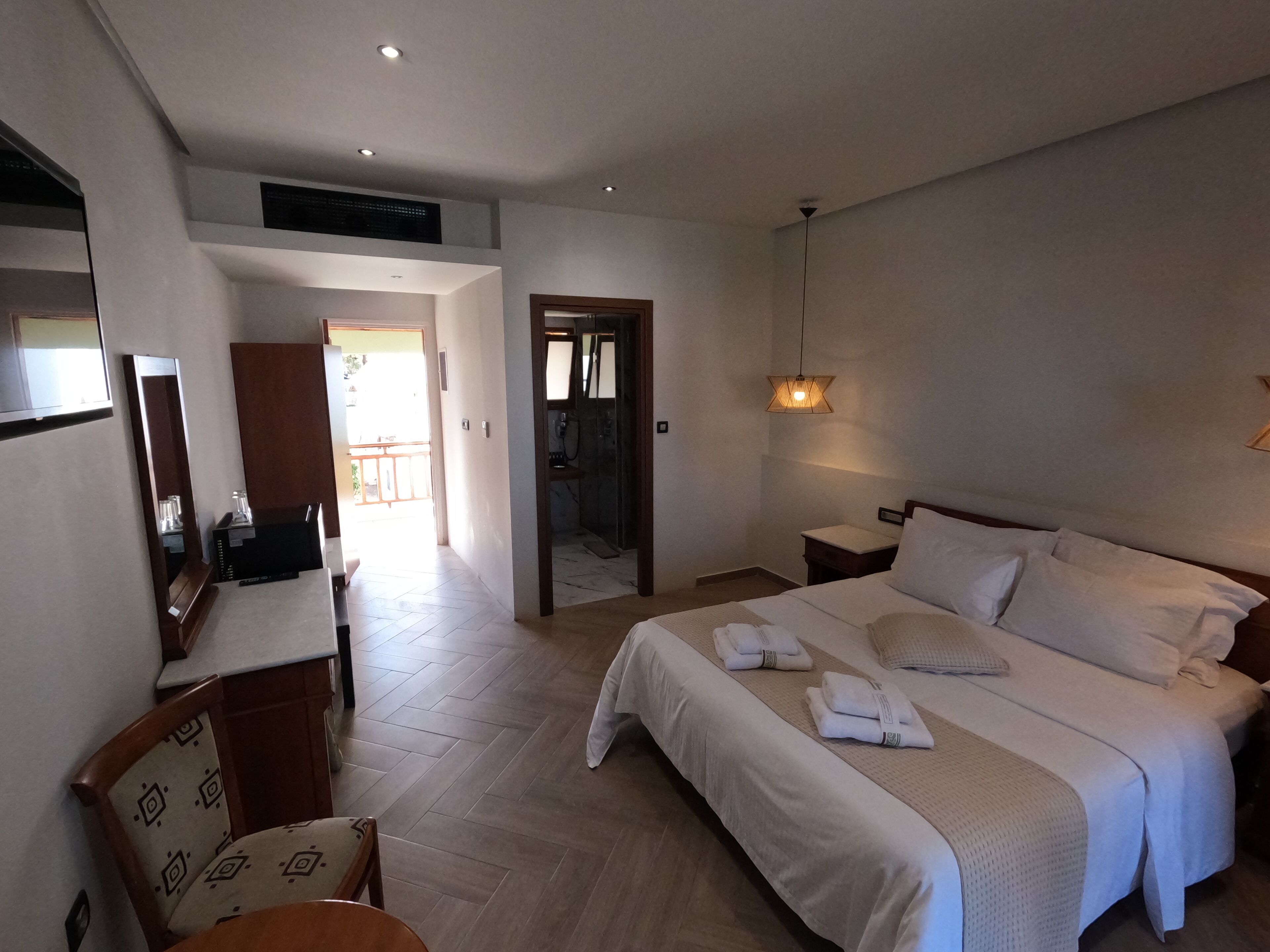 Une chambre d’hôtel avec un grand lit, des tables de chevet, un bureau avec une chaise, un miroir et un téléviseur.