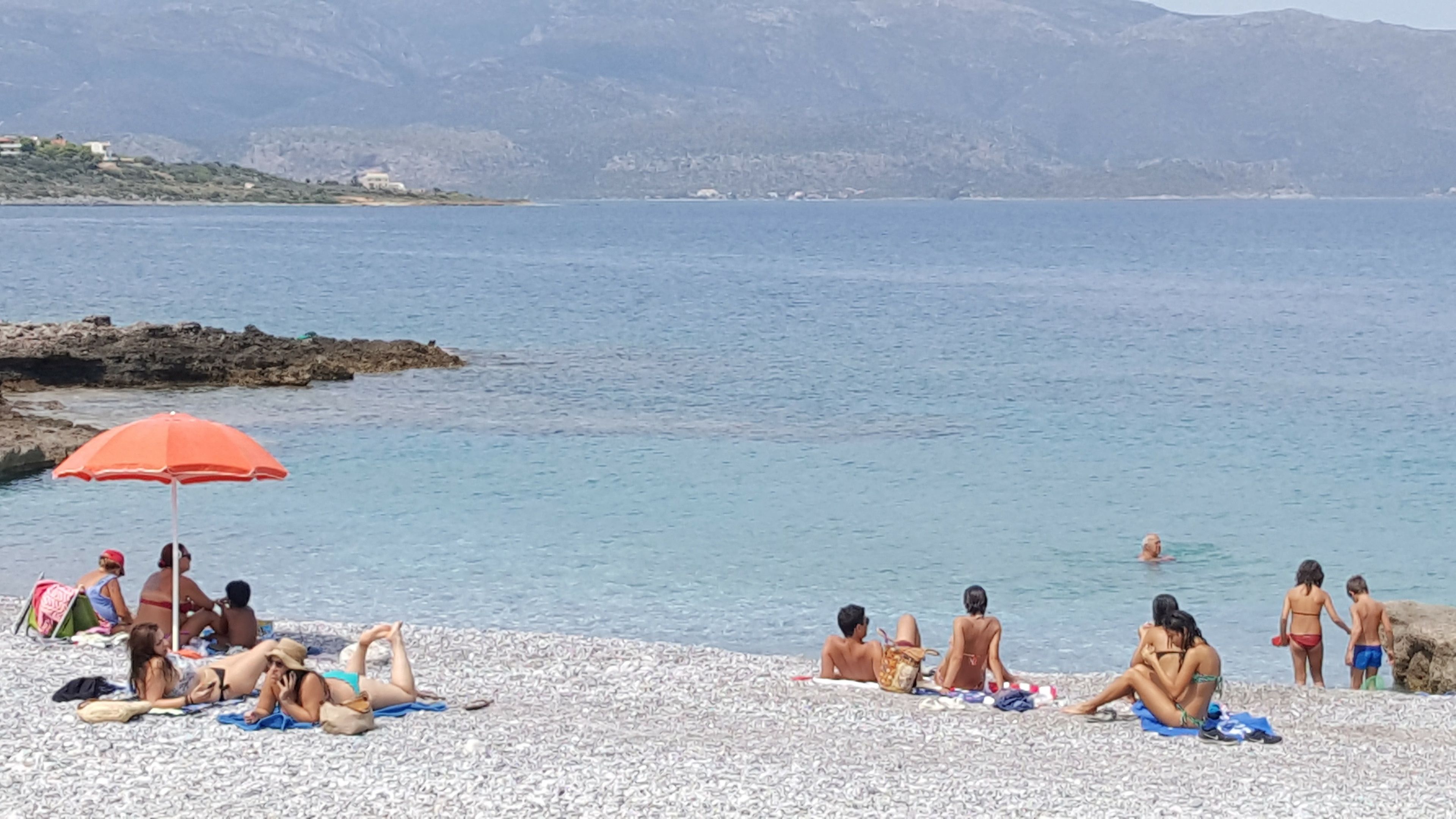 Una playa con gente tomando el sol y nadando.