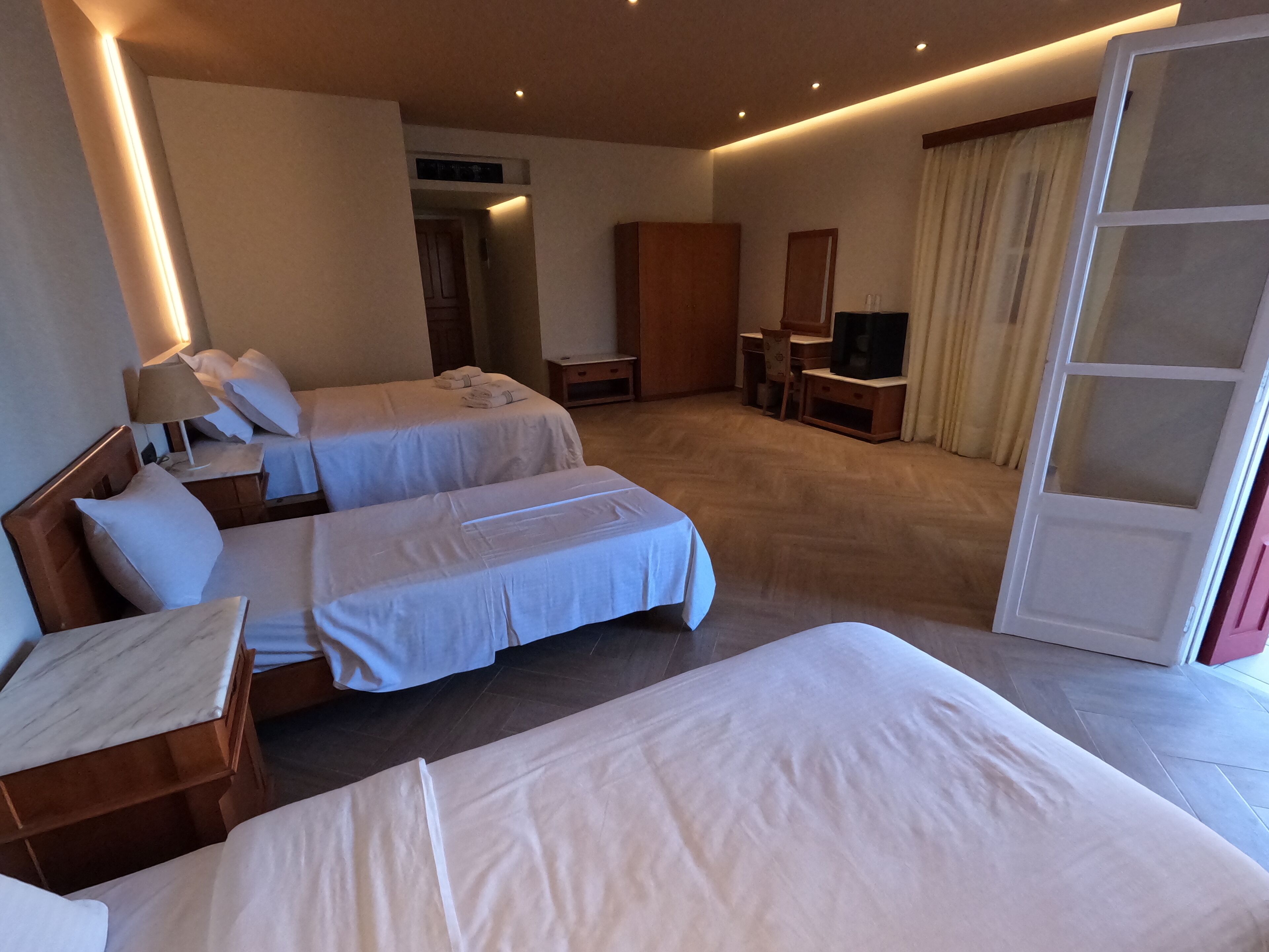 Habitación de hotel con dos camas, un escritorio, una silla, un televisor y una puerta corredera.