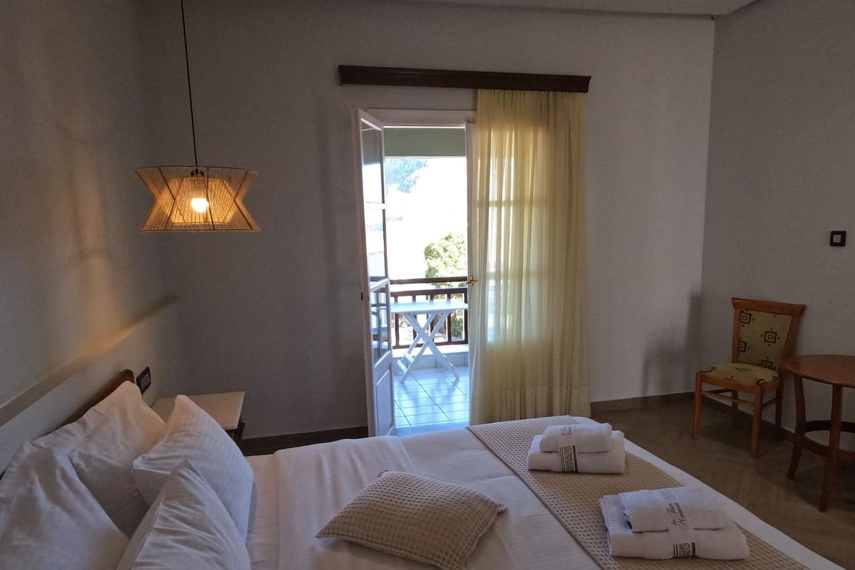 A hotel room with a bed, a chair, a table, and a view of the outside balcony.