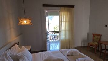 A hotel room with a bed, a chair, a table, and a view of the outside balcony.
