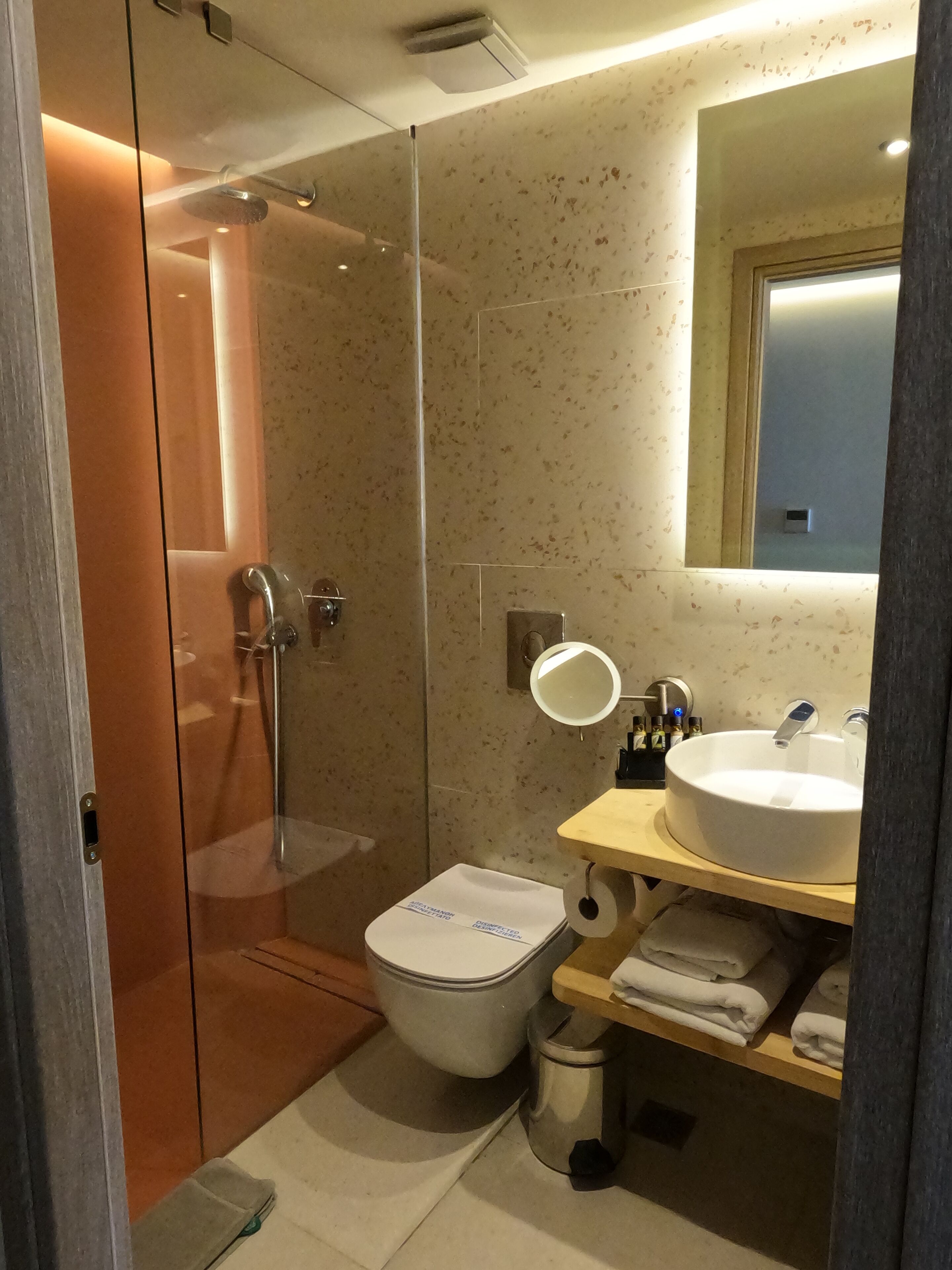 Un baño moderno con ducha envuelta en vidrio, inodoro y lavamanos con espejo superior.