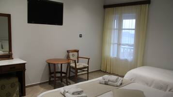 Una habitación de hotel con cama, escritorio, silla, televisor y ventana con cortinas.