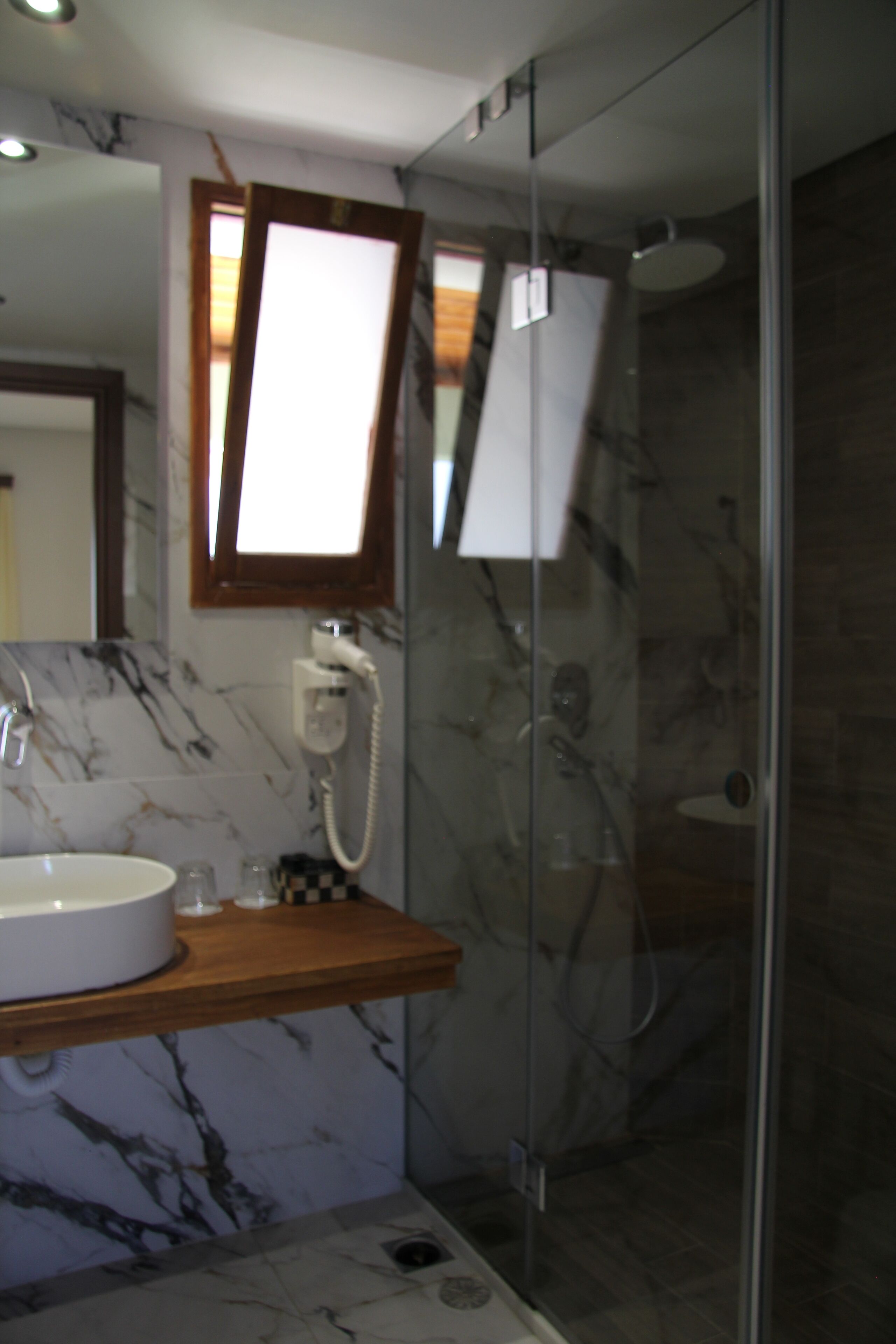 A modern bathroom with a marble sink, a glass shower enclosure, and a visible telephone.