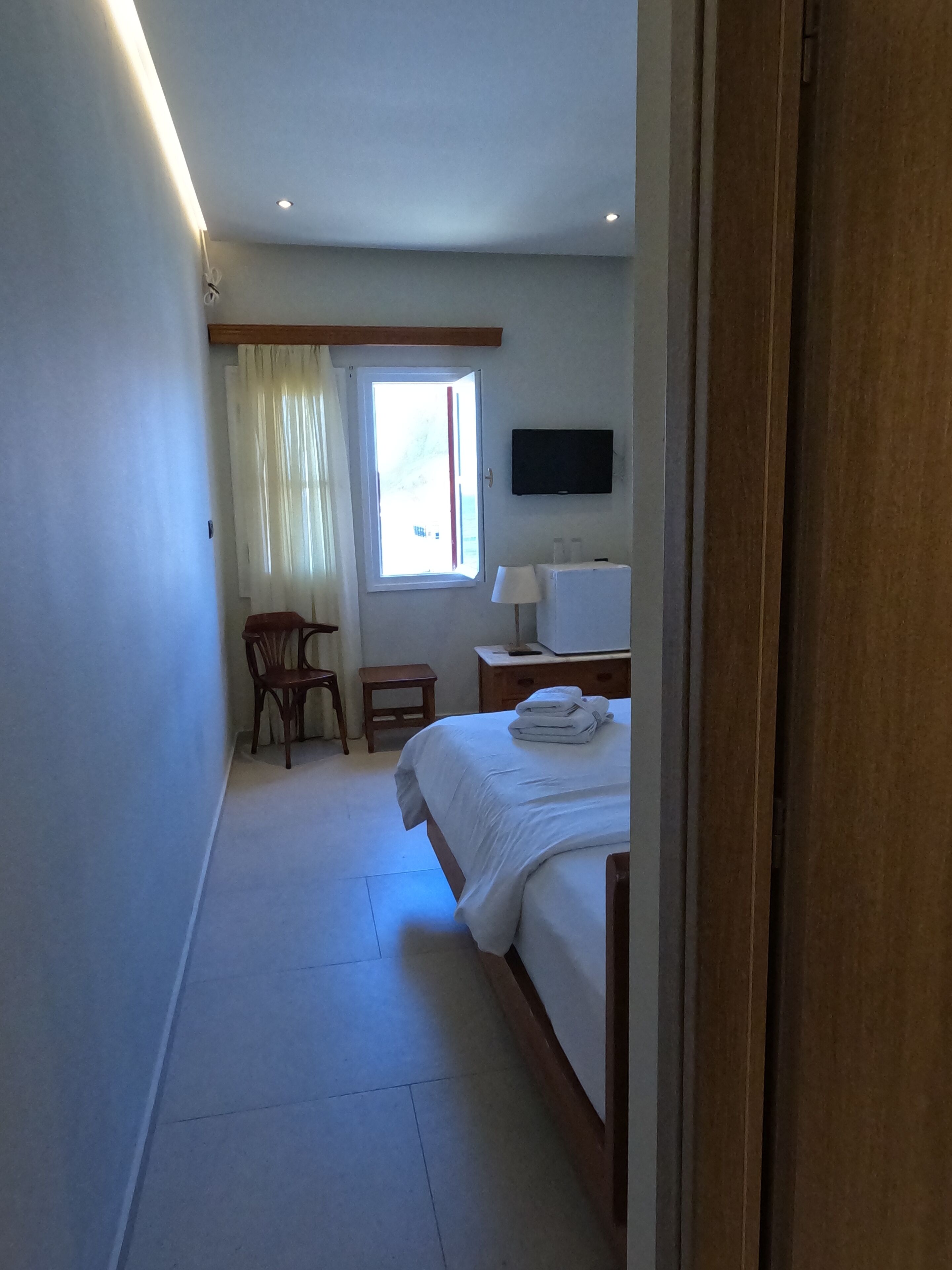 Habitación de hotel con cama, escritorio, silla, televisor y ventana con cortinas.