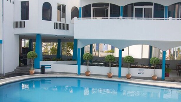 A swimming pool with a clear blue water surface, surrounded by a white building with blue accents and multiple windows. - Dorados Acapulco (Acapulco)