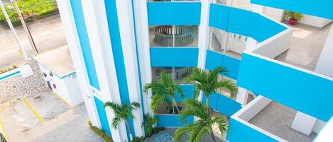 A multi-level building with blue and white exterior walls, a central atrium with a spiral staircase, and palm trees.