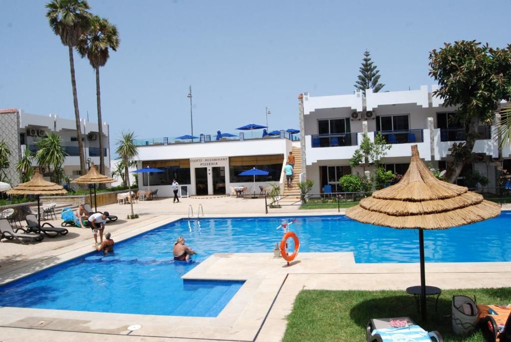 A swimming pool with lounge chairs and umbrellas, a lifebuoy, and a building with a sign for a coffee restaurant and pizzeria.
