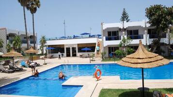 A swimming pool with lounge chairs and umbrellas, a lifebuoy, and a building with a sign for a coffee restaurant and pizzeria.
