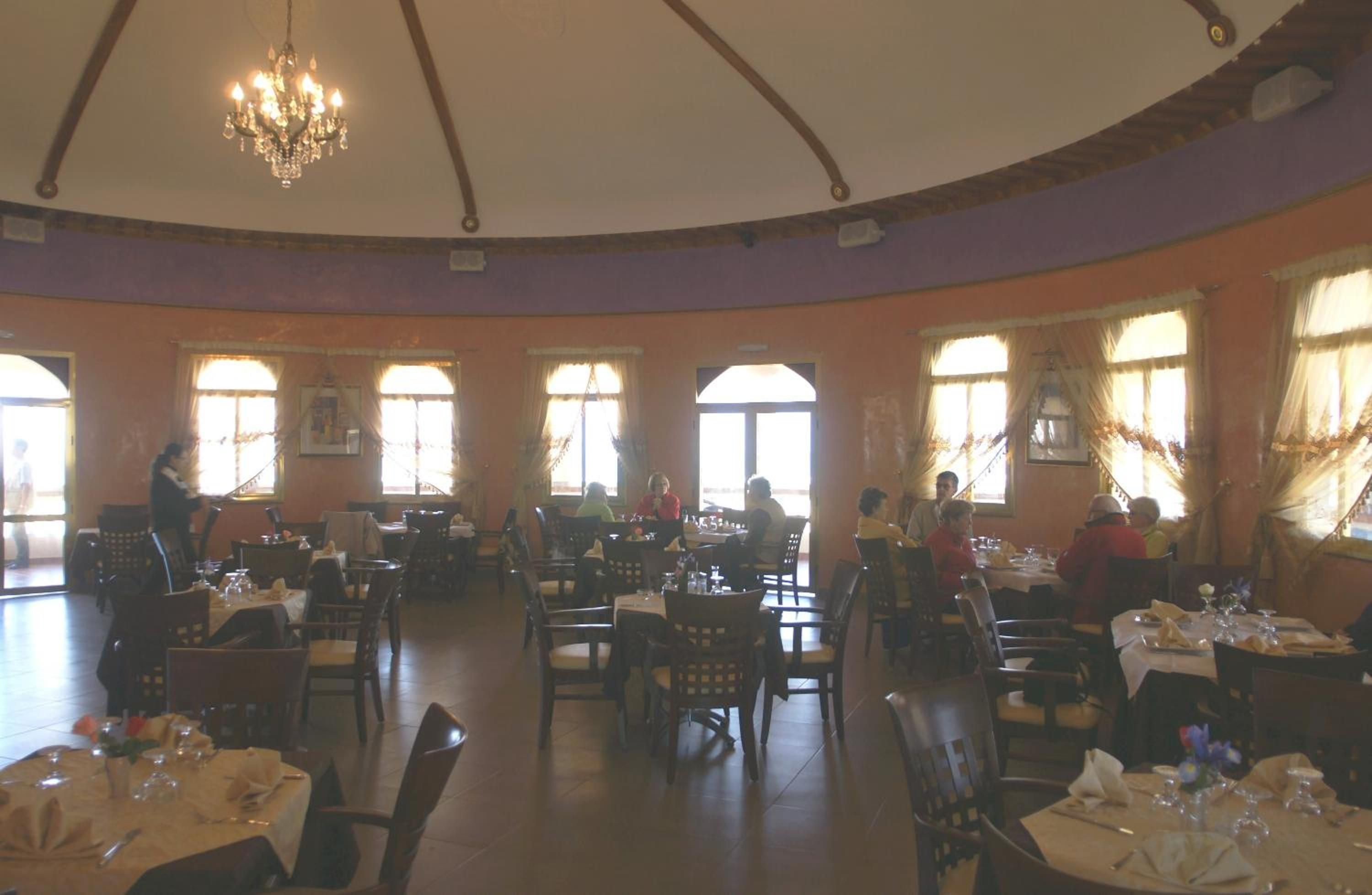 A restaurant with multiple tables and chairs, large windows, and a chandelier.
