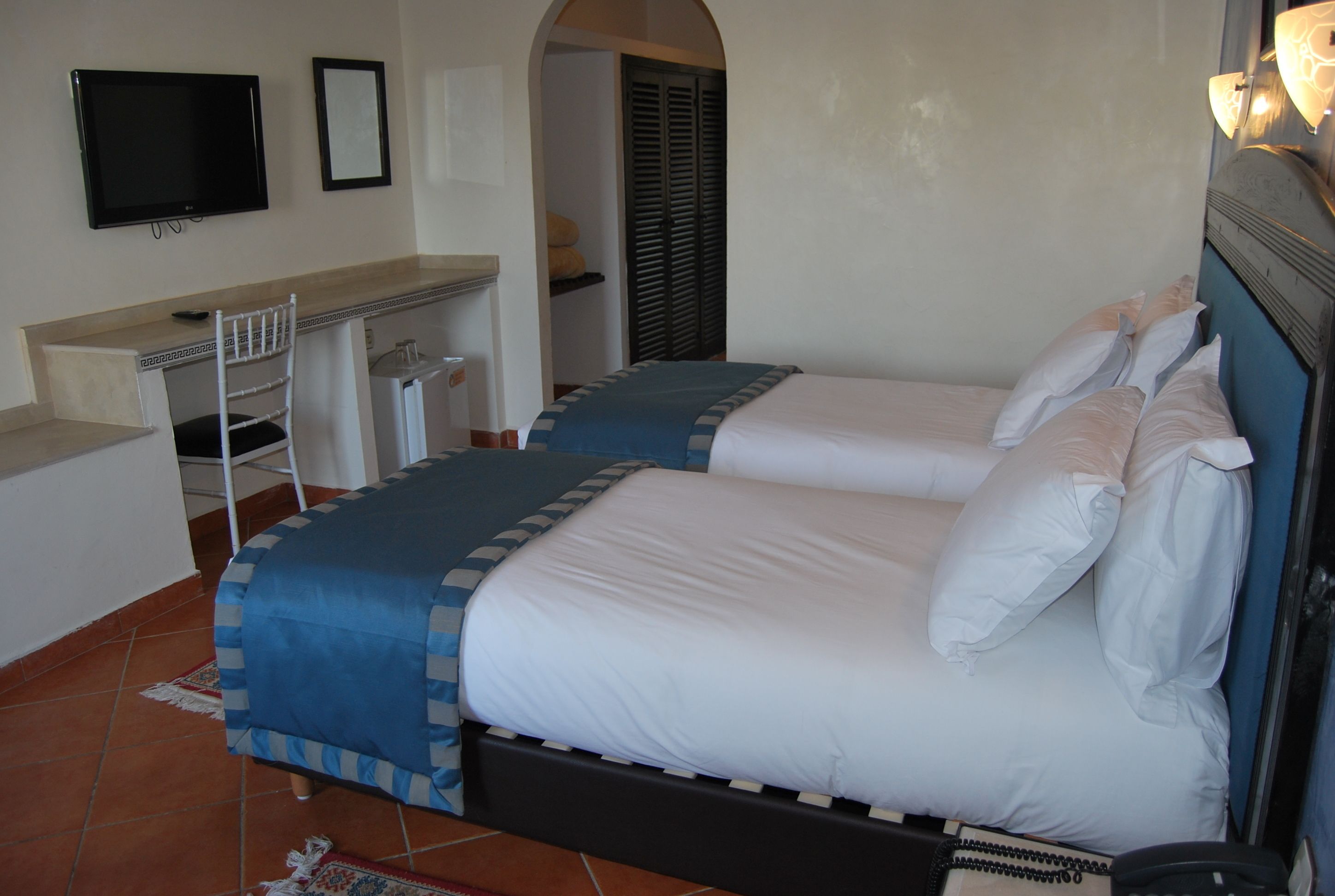A bedroom with two beds, a desk, a chair, a TV, and a wardrobe.