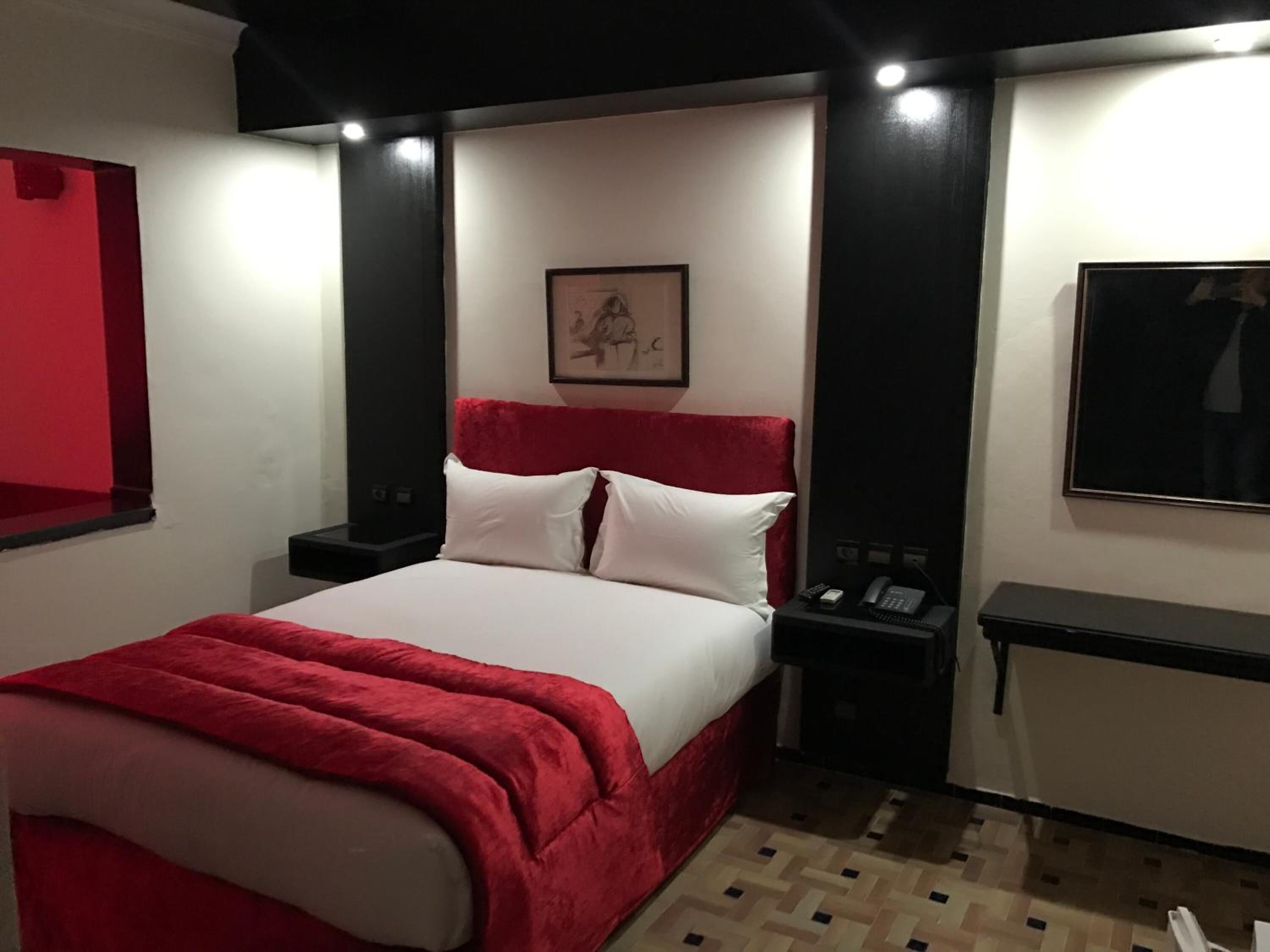 Una habitación de hotel con una cama, mesitas de noche, un teléfono y un cuadro en la pared.