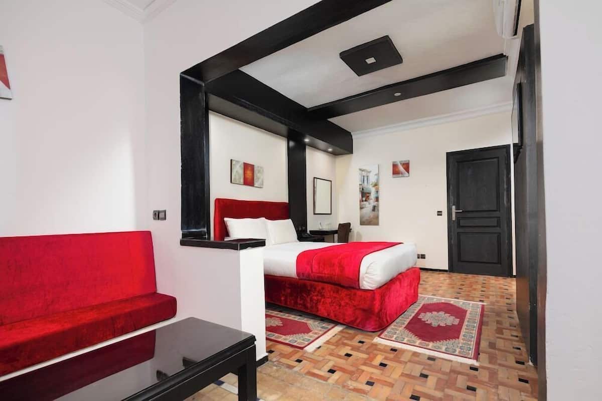A hotel room with a bed, a red sofa, a small table, a mirror, and a door.