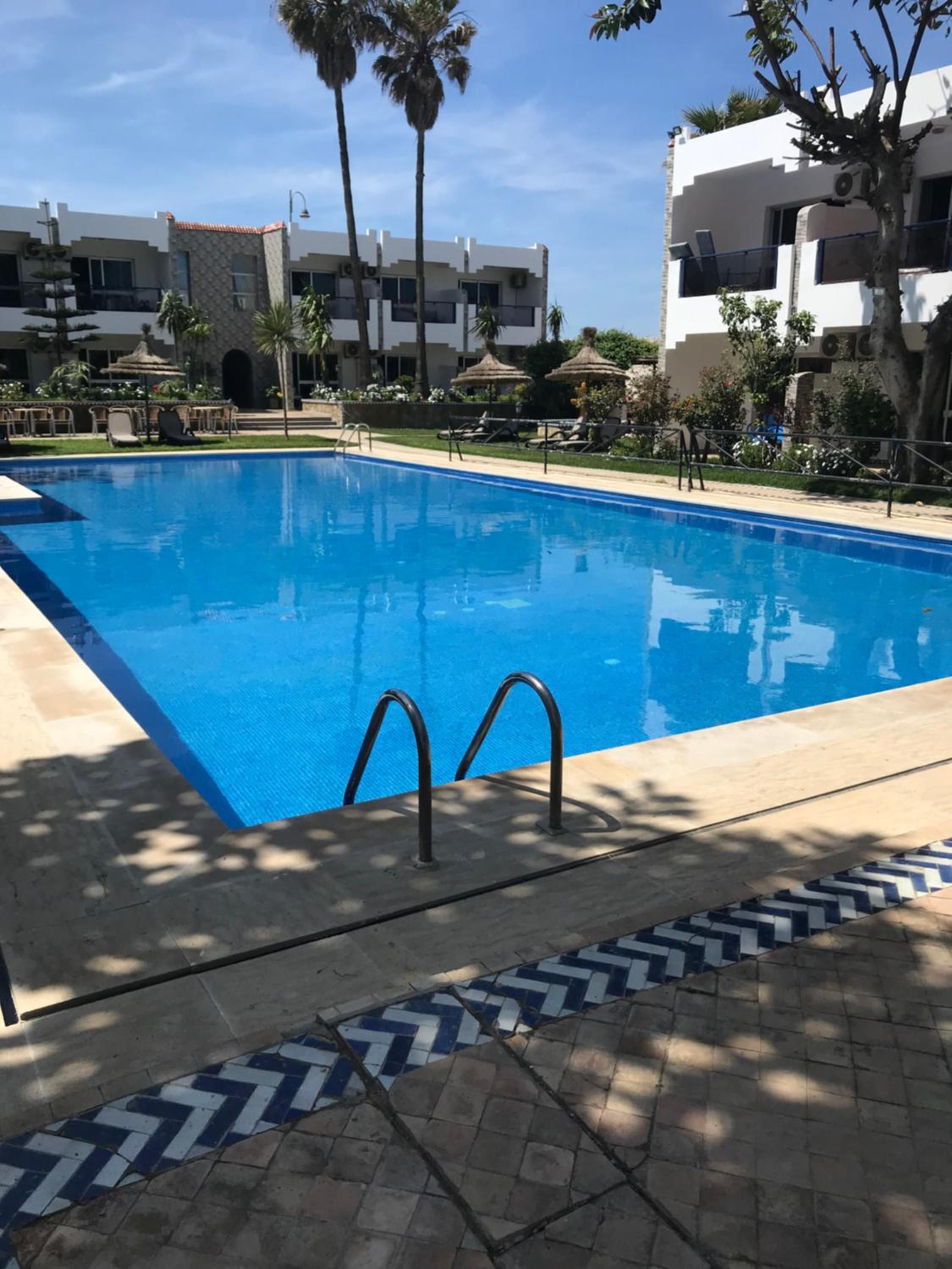 Ein Swimmingpool mit glasklarer, blauer Wasseroberfläche, umgeben von Liegestühlen und Palmen.