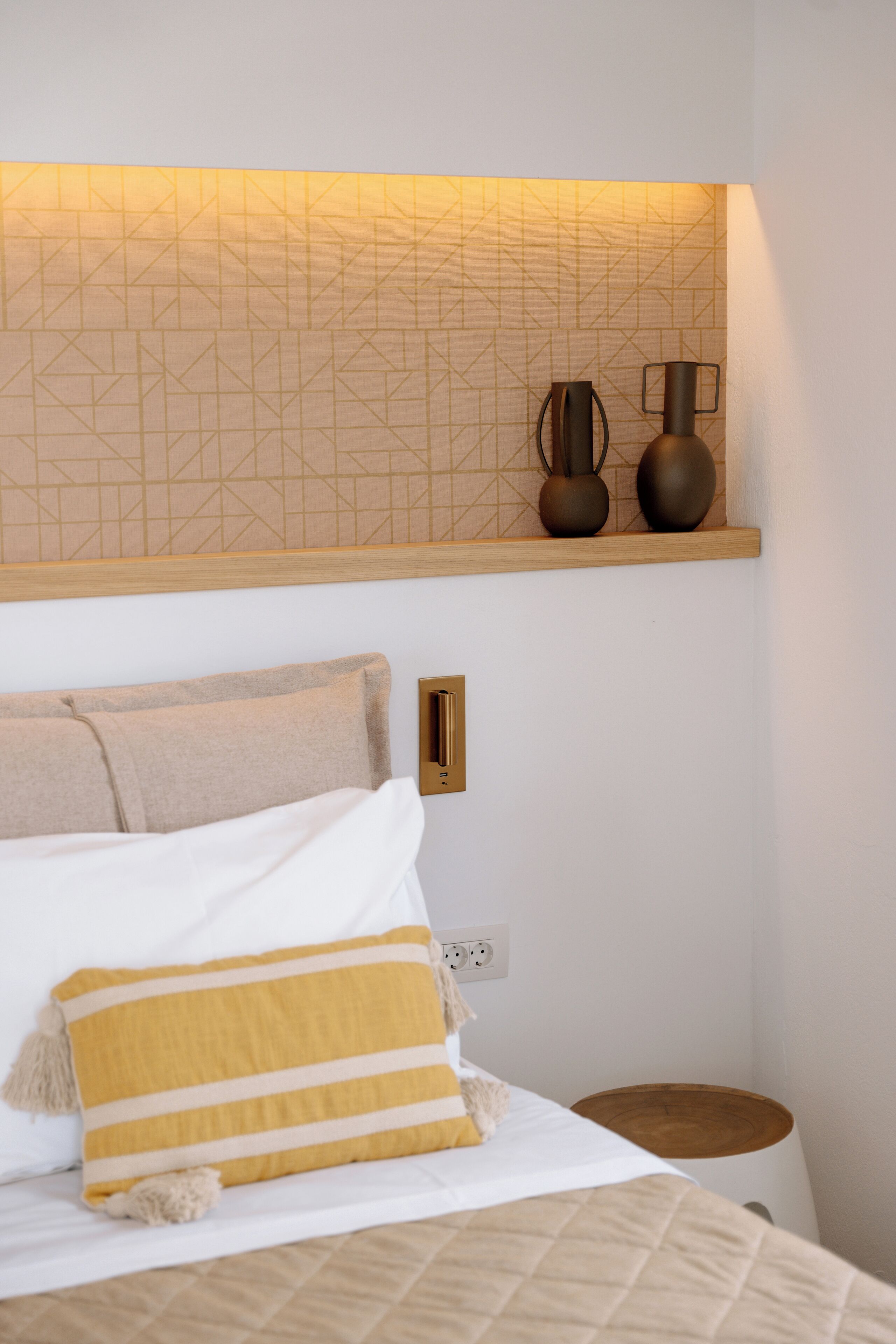 A neatly arranged bedroom with a bed, pillows, a bedside table, and a wall-mounted shelf with decorative items.