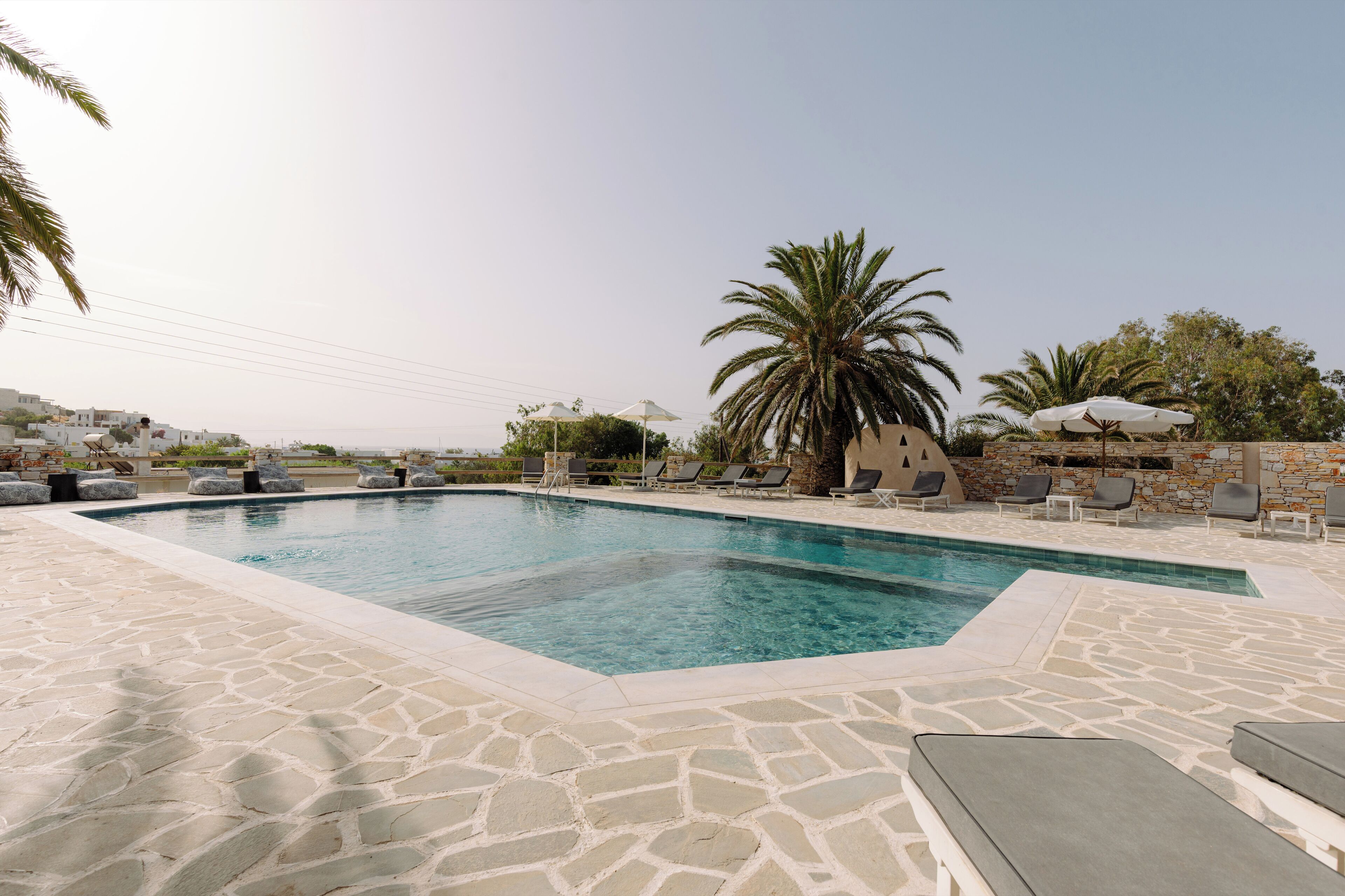 Una piscina con baldosas de piedra, sillas de descanso y palmeras.