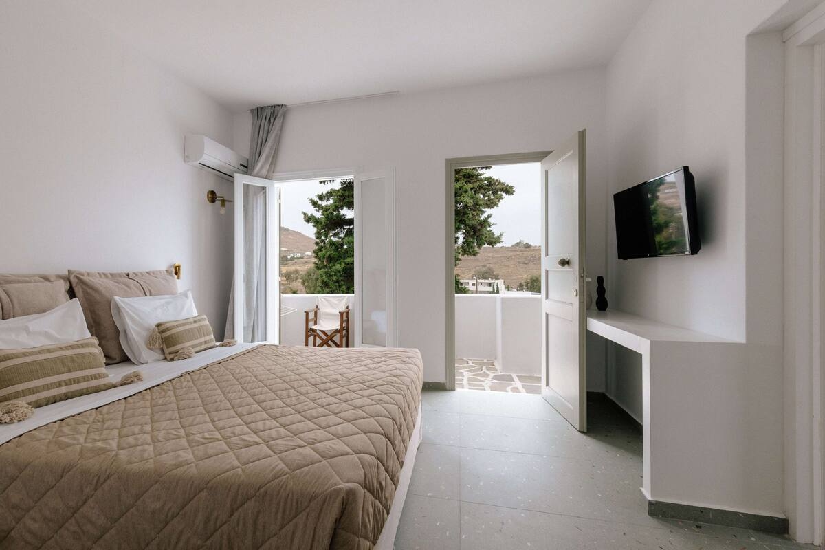 A bedroom with a bed, a TV mounted on the wall, and a balcony door leading to an outdoor area.