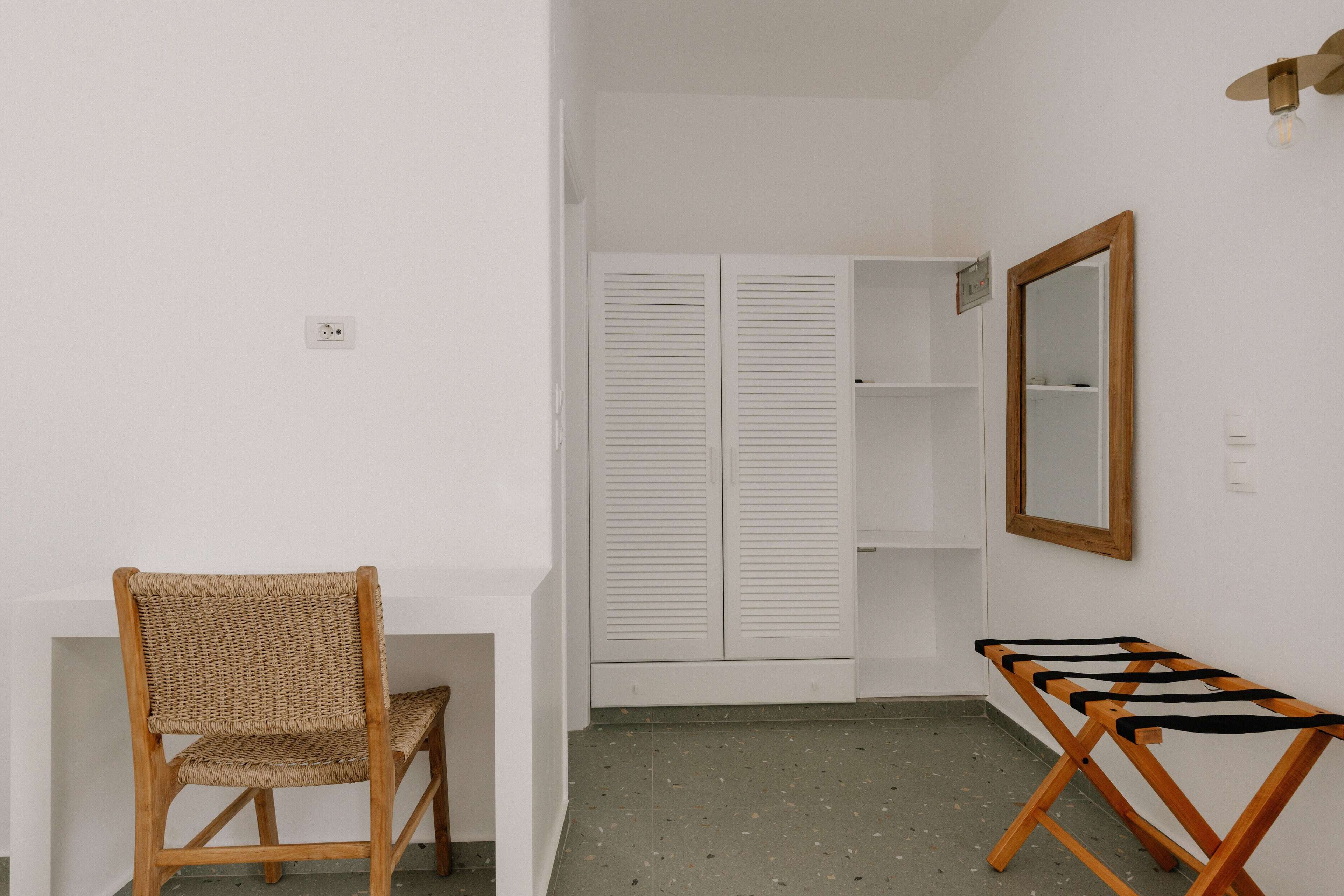 A room with a wicker chair, a wooden table, a wardrobe, and a mirror.