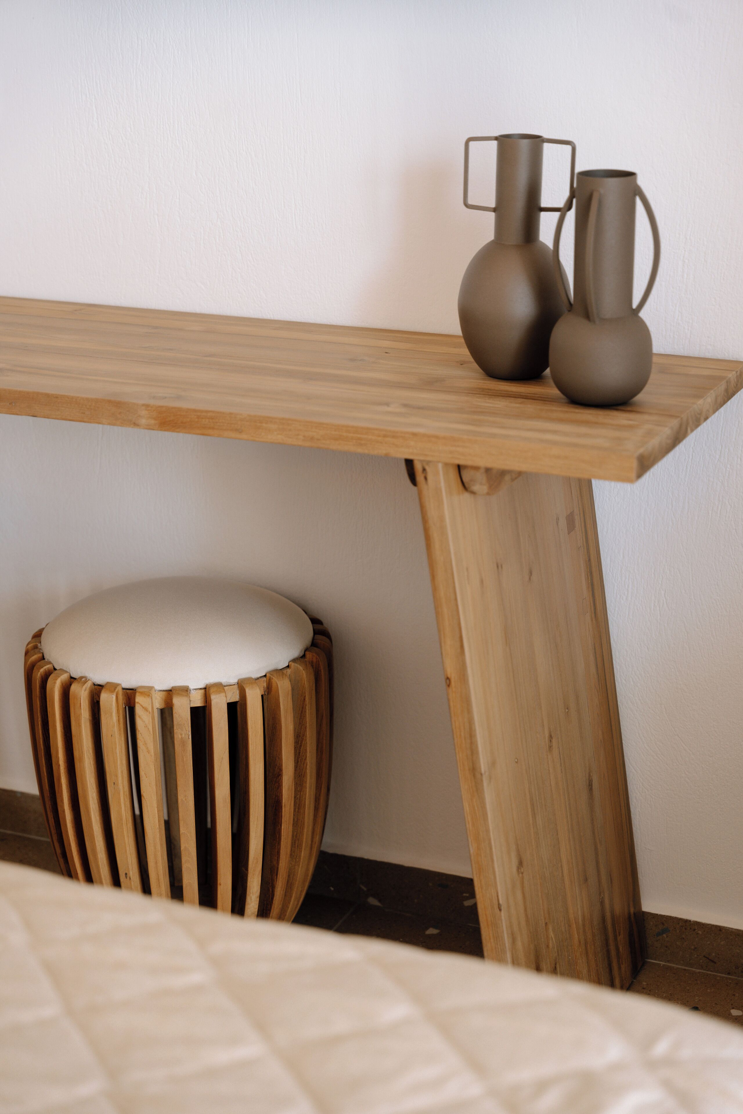 A wooden table with two vases and a stool with a cushioned seat.