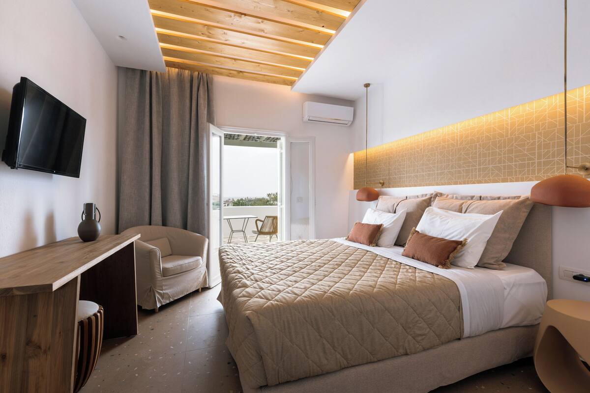 A bedroom with a bed, a desk, a chair, a TV, and a balcony.