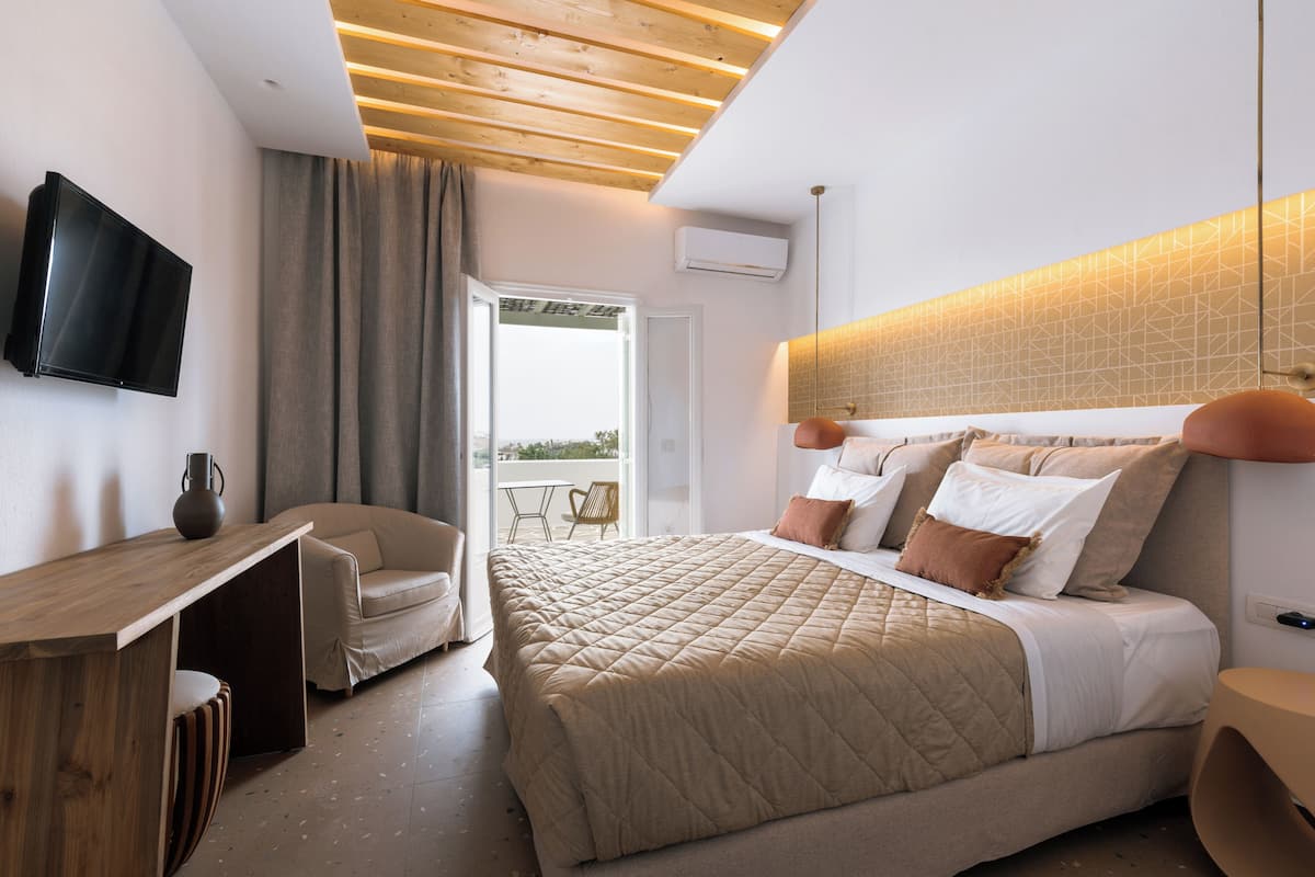 A bedroom with a bed, a desk, a chair, a television, and an air conditioning unit.