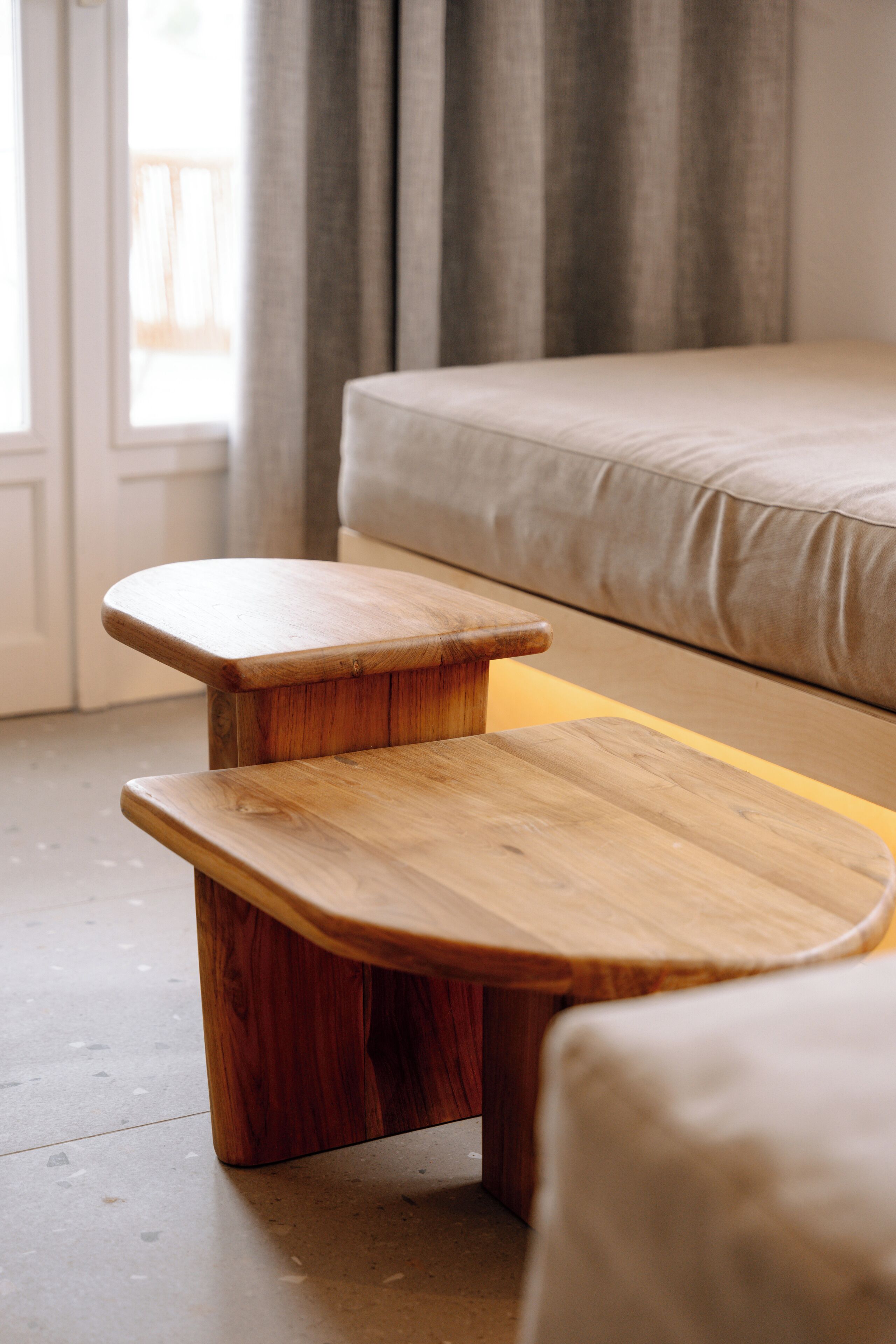 Un banc en bois avec un coussin, dans une pièce où se trouvent un lit et des rideaux.