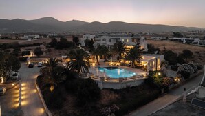 A modern villa with a swimming pool, surrounded by palm trees and a well-lit driveway.