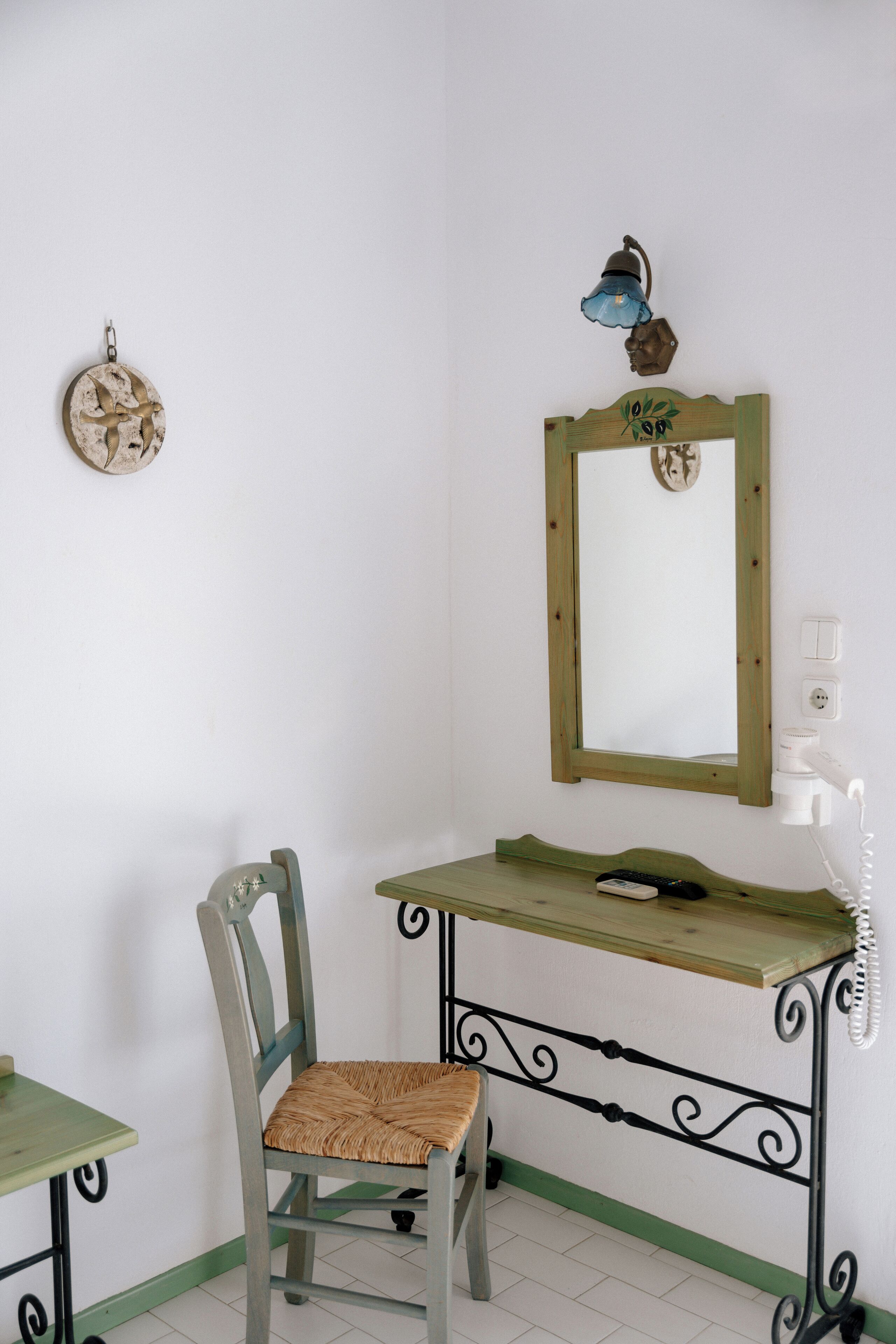 A room with a wooden chair, a small table, a mirror, and a wall-mounted light fixture.