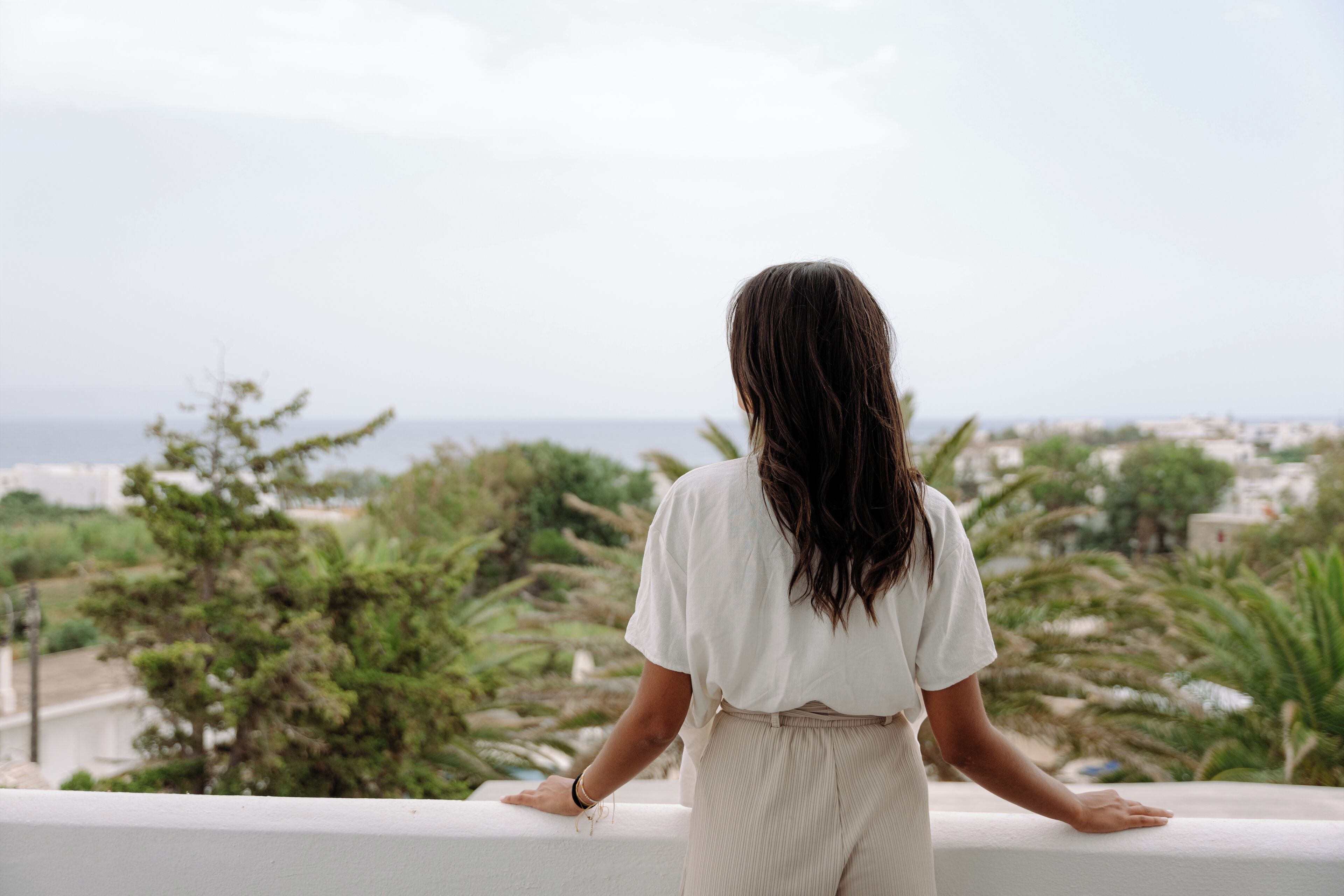 A person standing on a balcony overlooking a coastal landscape with trees and buildings.