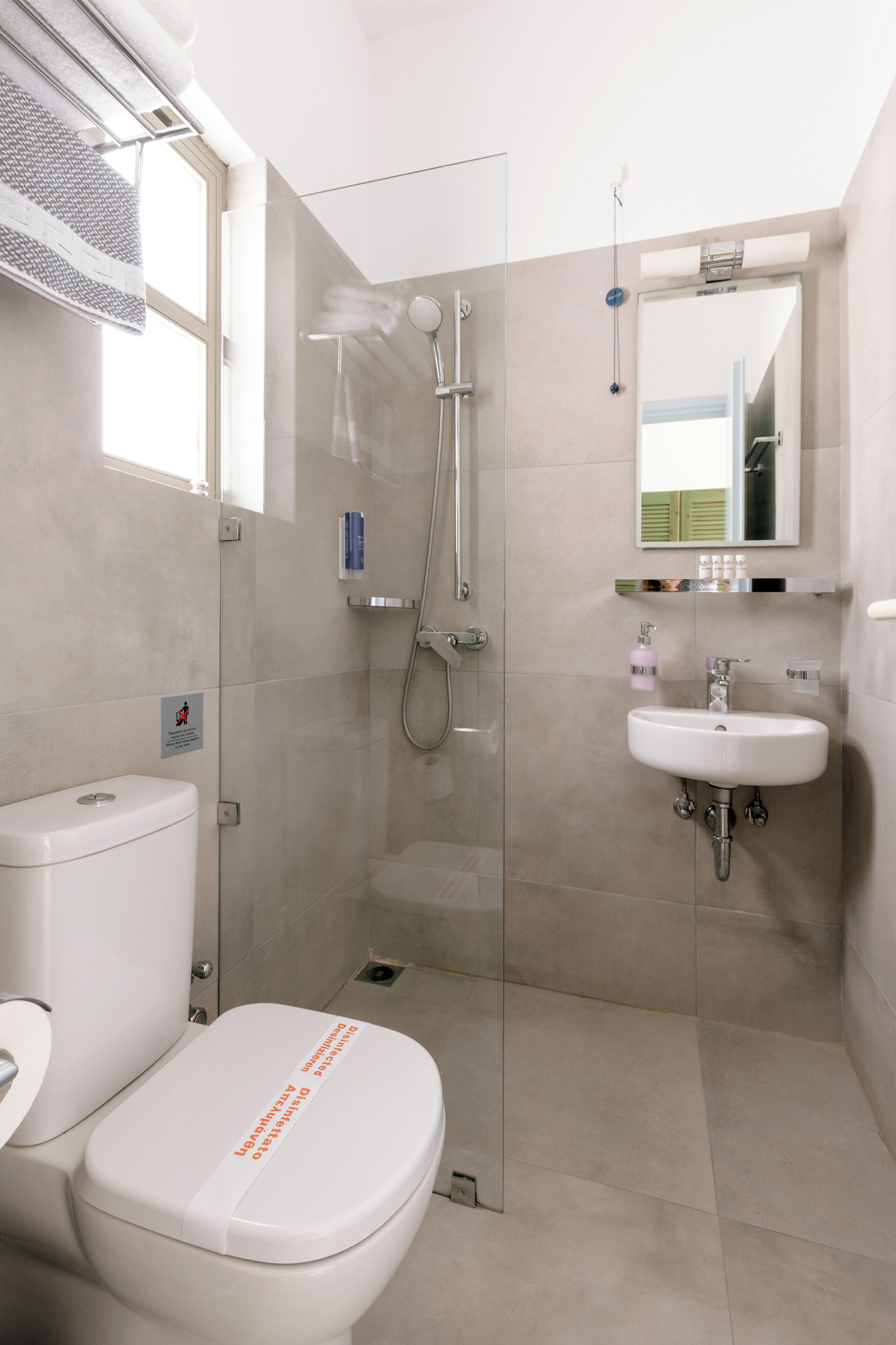 A modern bathroom with a toilet, a glass-enclosed shower, and a sink with a mirror above it.