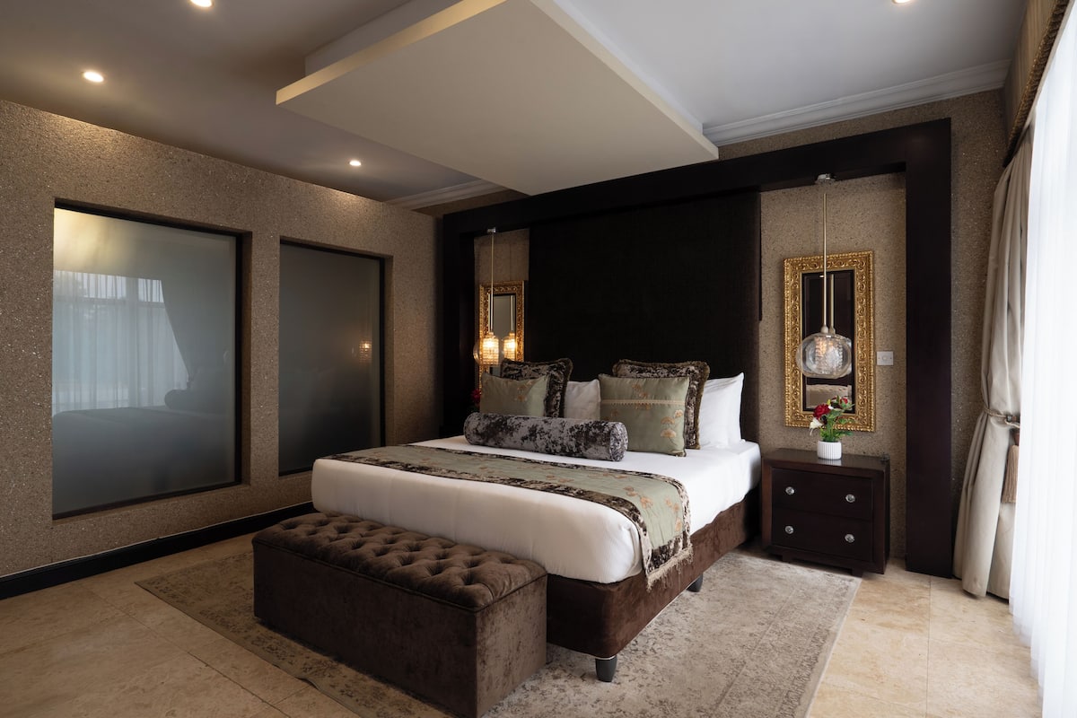A bedroom with a large bed, a nightstand, a mirror, and a window with curtains.