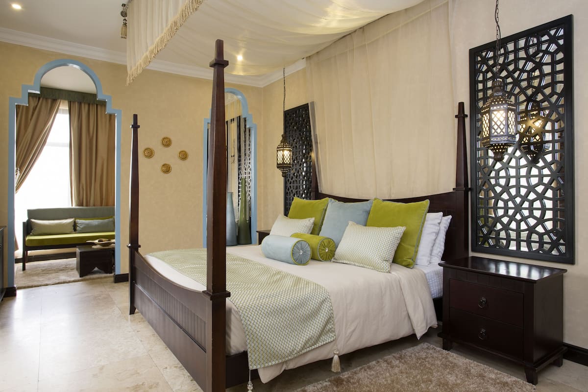 A four-poster bed with a wooden frame, a nightstand with drawers, and a decorative screen with a hanging lantern.