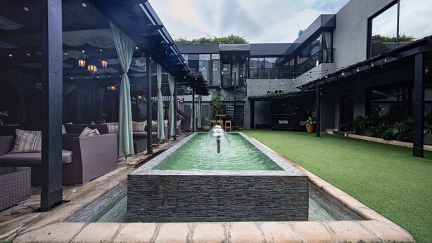 A modern outdoor pool area with a stone border, surrounded by seating and greenery. - Villa Monticello (Accra)