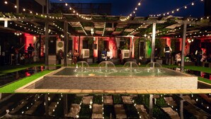 An outdoor patio area with a central water feature, string lights, and seating arrangements. - Villa Monticello (Accra)