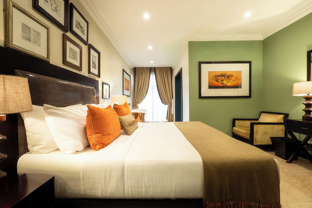 A neatly arranged hotel room with a large bed, a chair, a desk, and framed pictures on the walls.