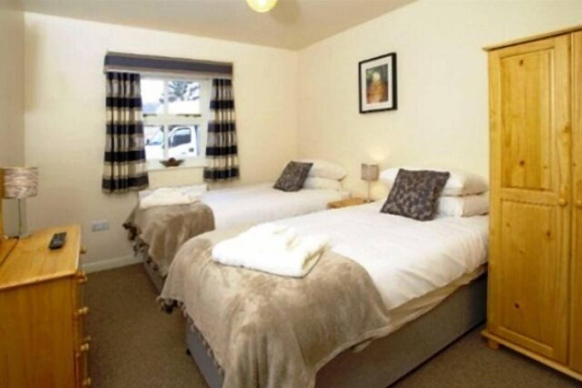 A room with two beds, a wooden wardrobe, a window with curtains, and a framed picture on the wall.