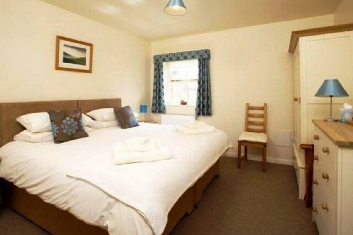 A bedroom with a bed, a chair, a dresser, and a window with curtains.