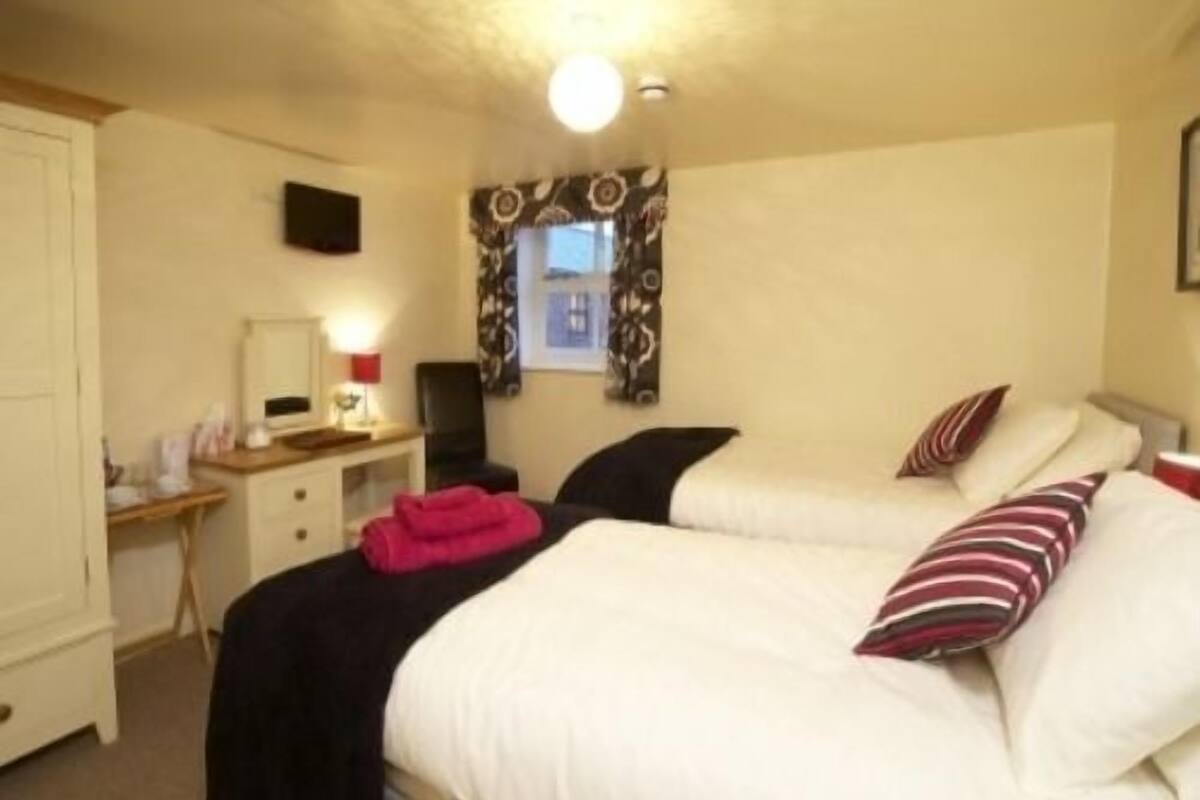 A hotel room with two beds, a desk, a chair, and a window with curtains.