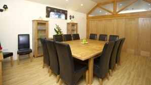 Une salle de conférence avec une table en bois et des chaises noires, une petite plante et un téléviseur fixé au mur.